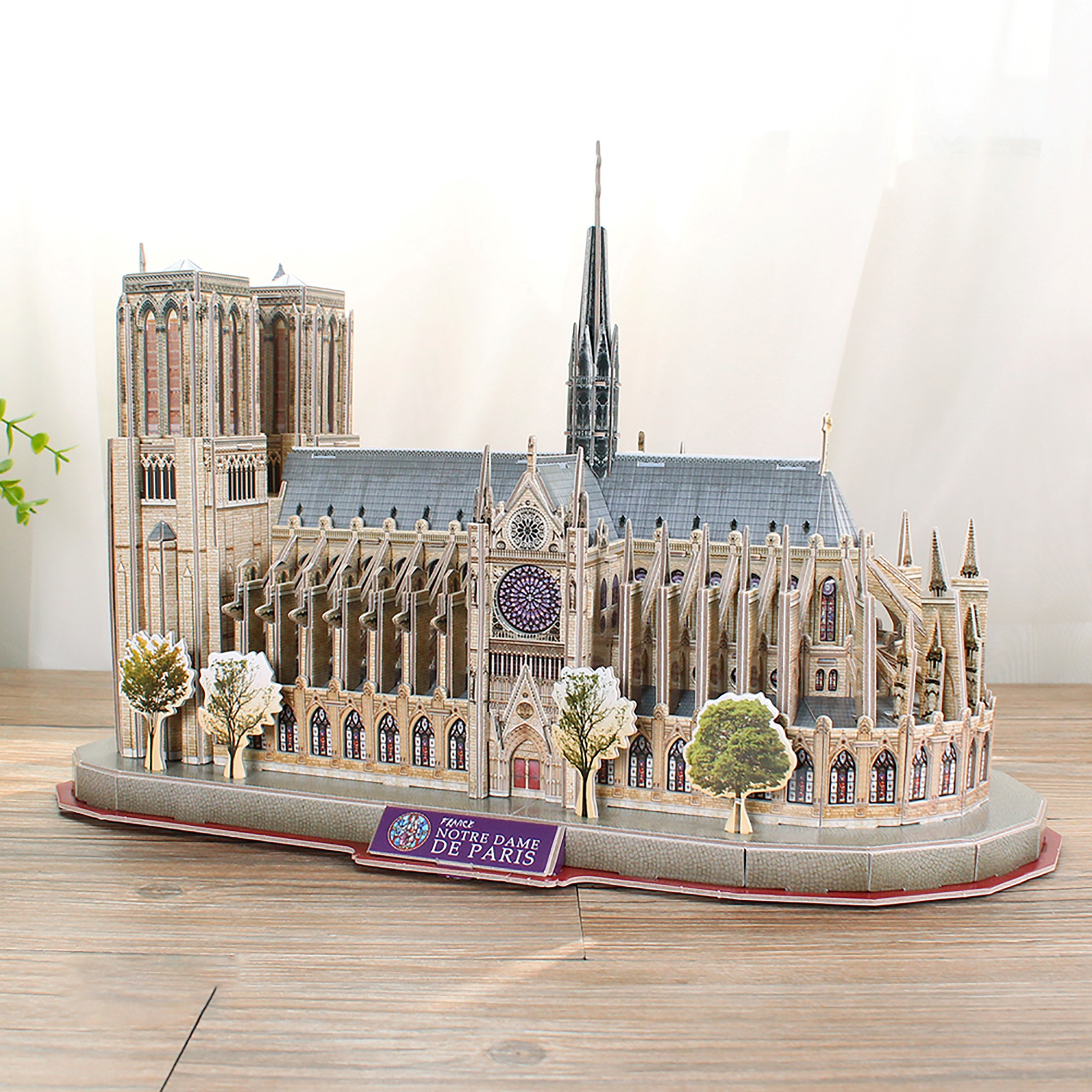 Puzzle 3D katedry Notre Dame, z drzewami i czerwoną podstawą, na tle okna.