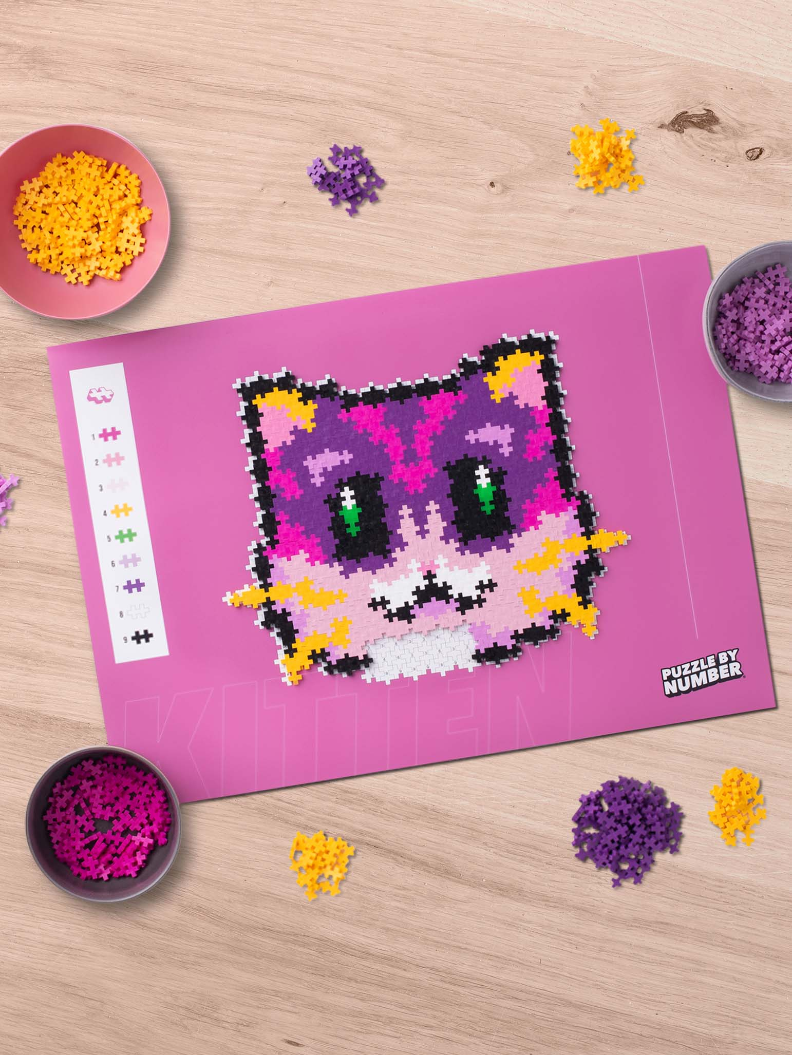 Układanka z kotkiem po numerach, z otaczającymi elementami. Różowe, żółte i fioletowe elementy są w miskach.