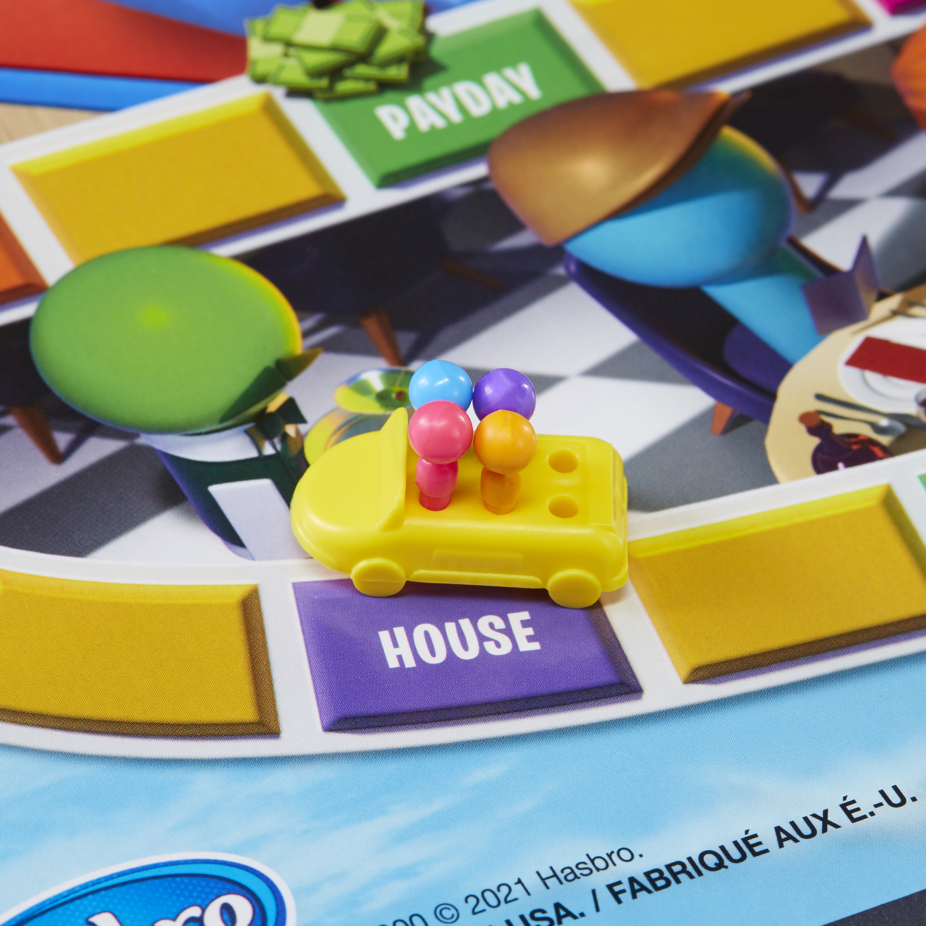 Een Life-spelbord met een auto en figuren erop. Omringende speelruimtes zijn zichtbaar.
