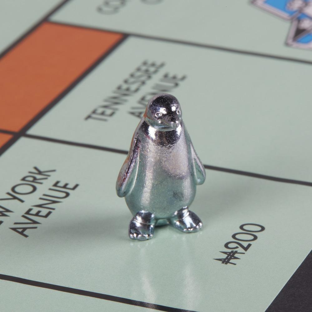Ficha de pingüino plateado de Monopoly en un tablero de Monopoly. El tablero tiene calles y valores.