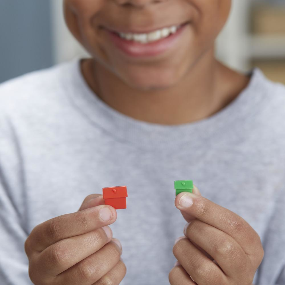 Un niño sostiene una casa roja y una casa verde de un juego de Monopoly.