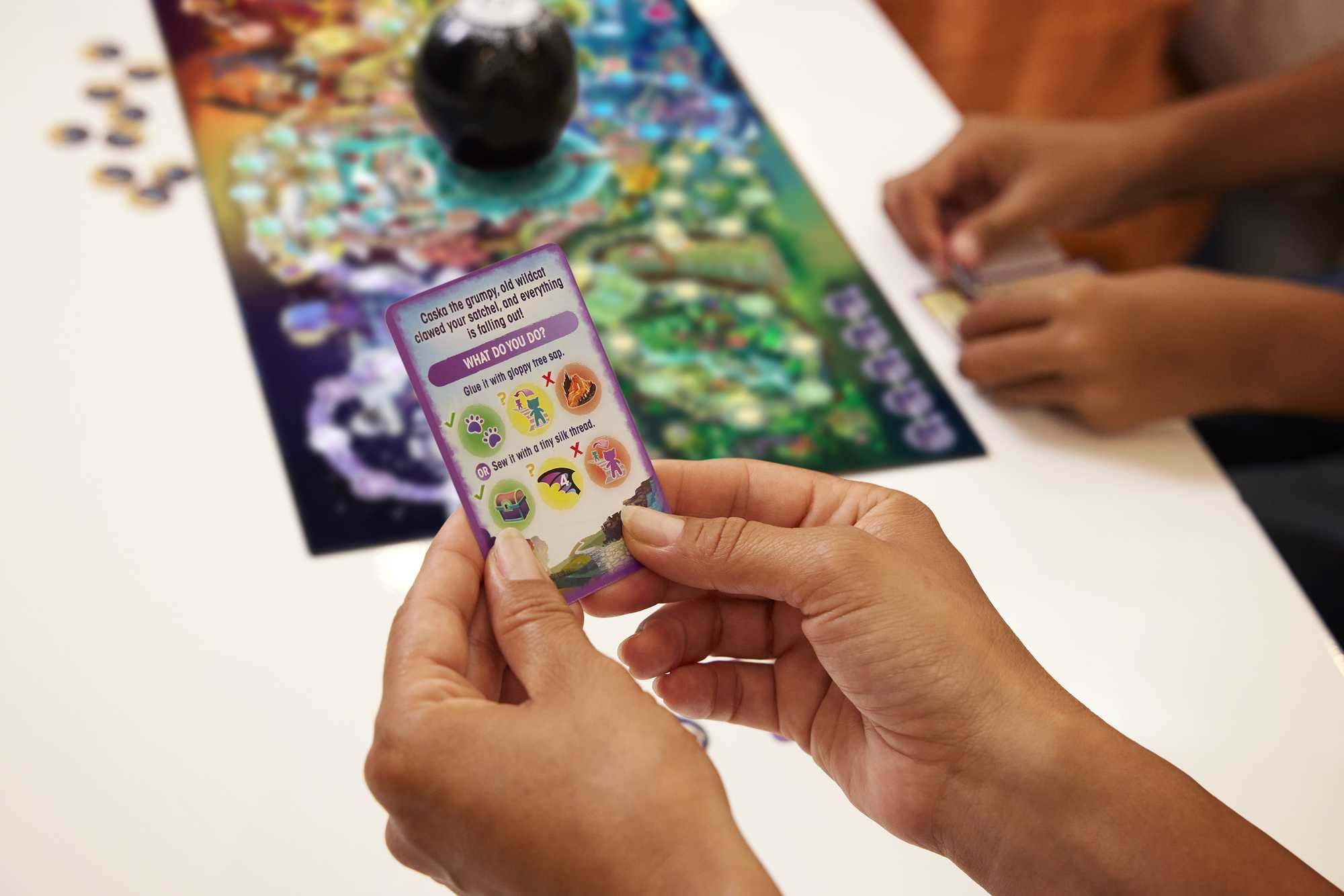 Een persoon houdt een kaart van een bordspel vast. Een bordspel en andere kaarten liggen op een tafel.