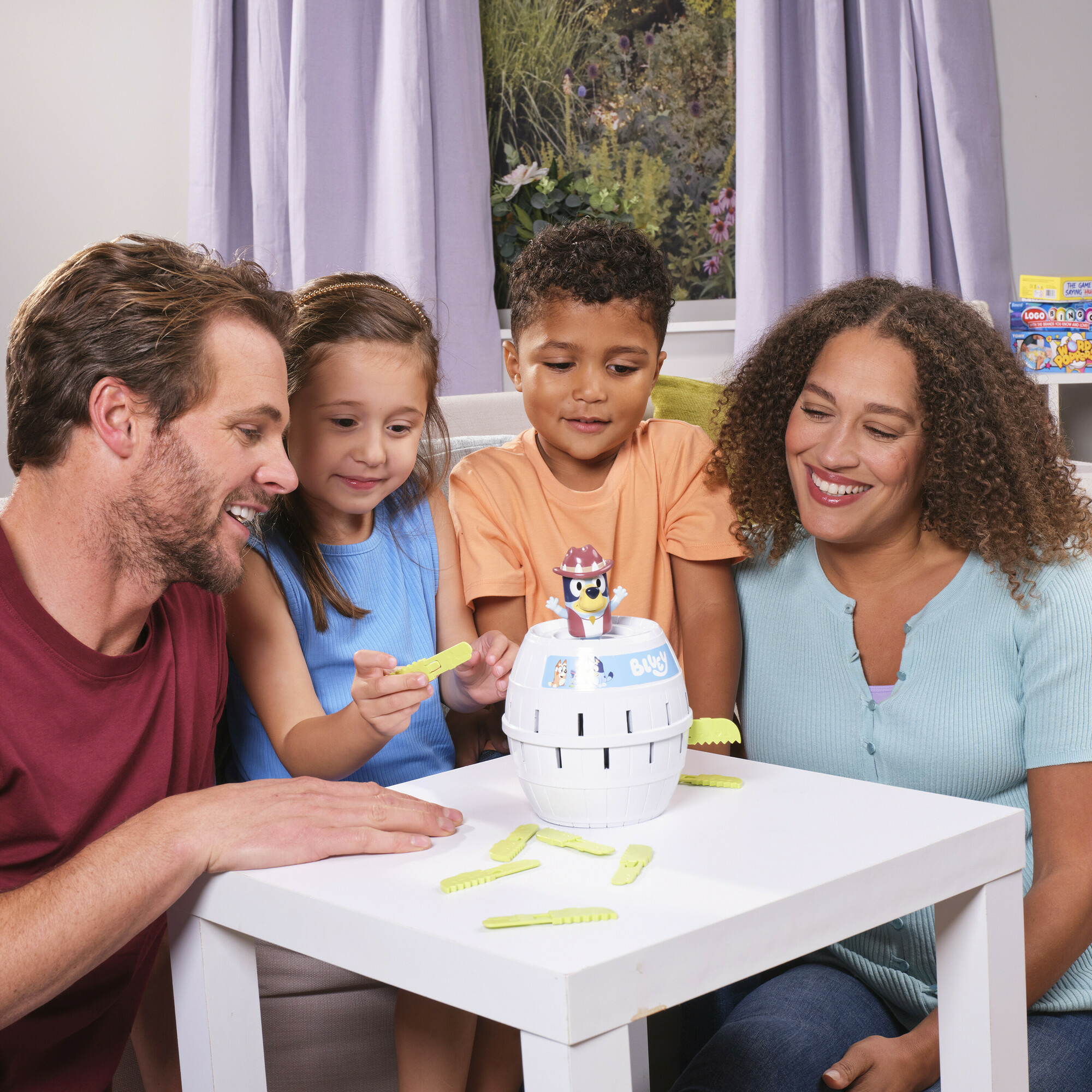 Familie spielt Pop Up Bluey-Spiel. Ein Fass und Hebel stehen auf dem Tisch.