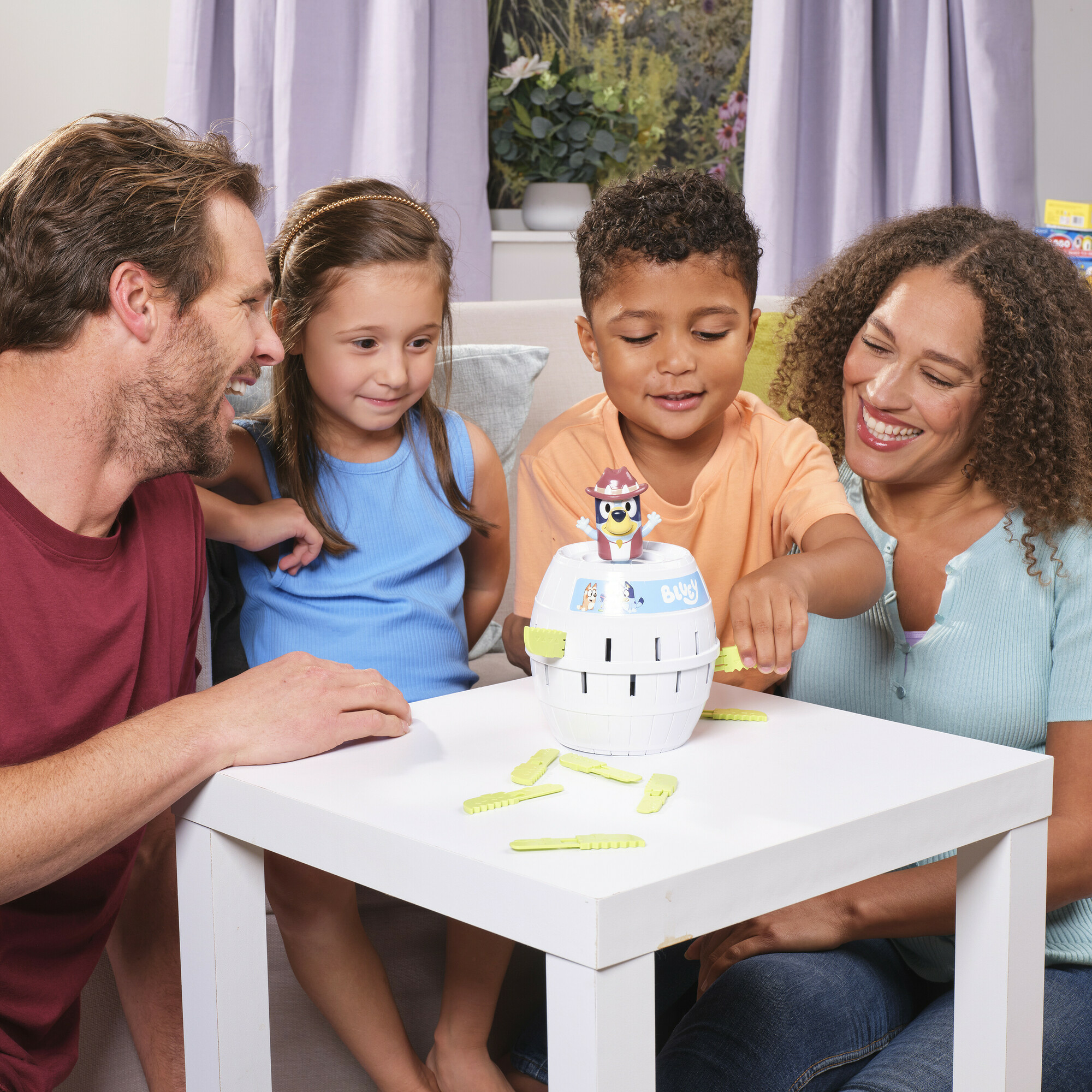 Eine Familie spielt zusammen ein Spiel. Personen sitzen um einen Tisch und interagieren mit einem Fassspiel.