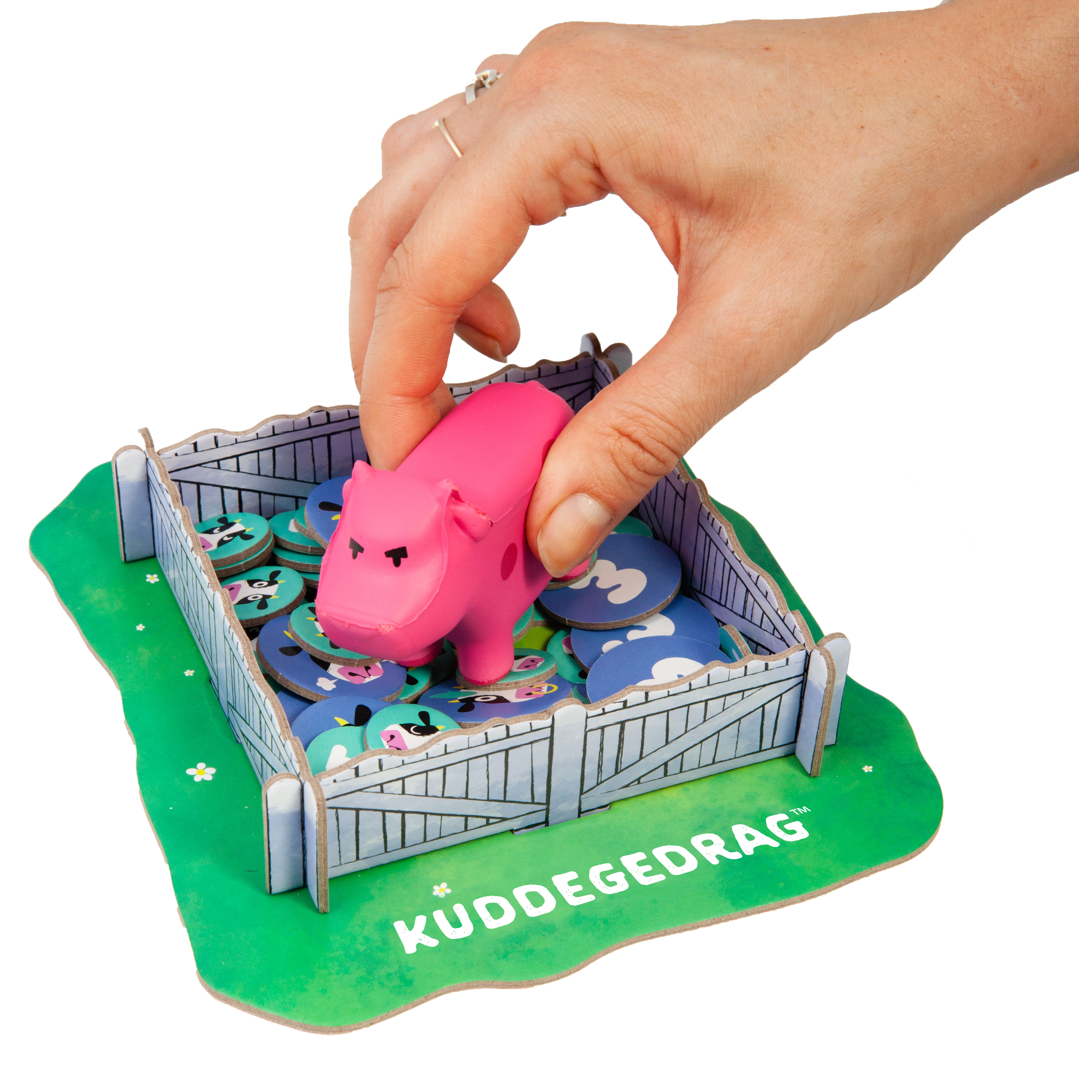Eine Hand platziert ein rosa Schwein in einem Gehege mit Karten. Das Gehege steht auf grünem Gras. Weißer Hintergrund.