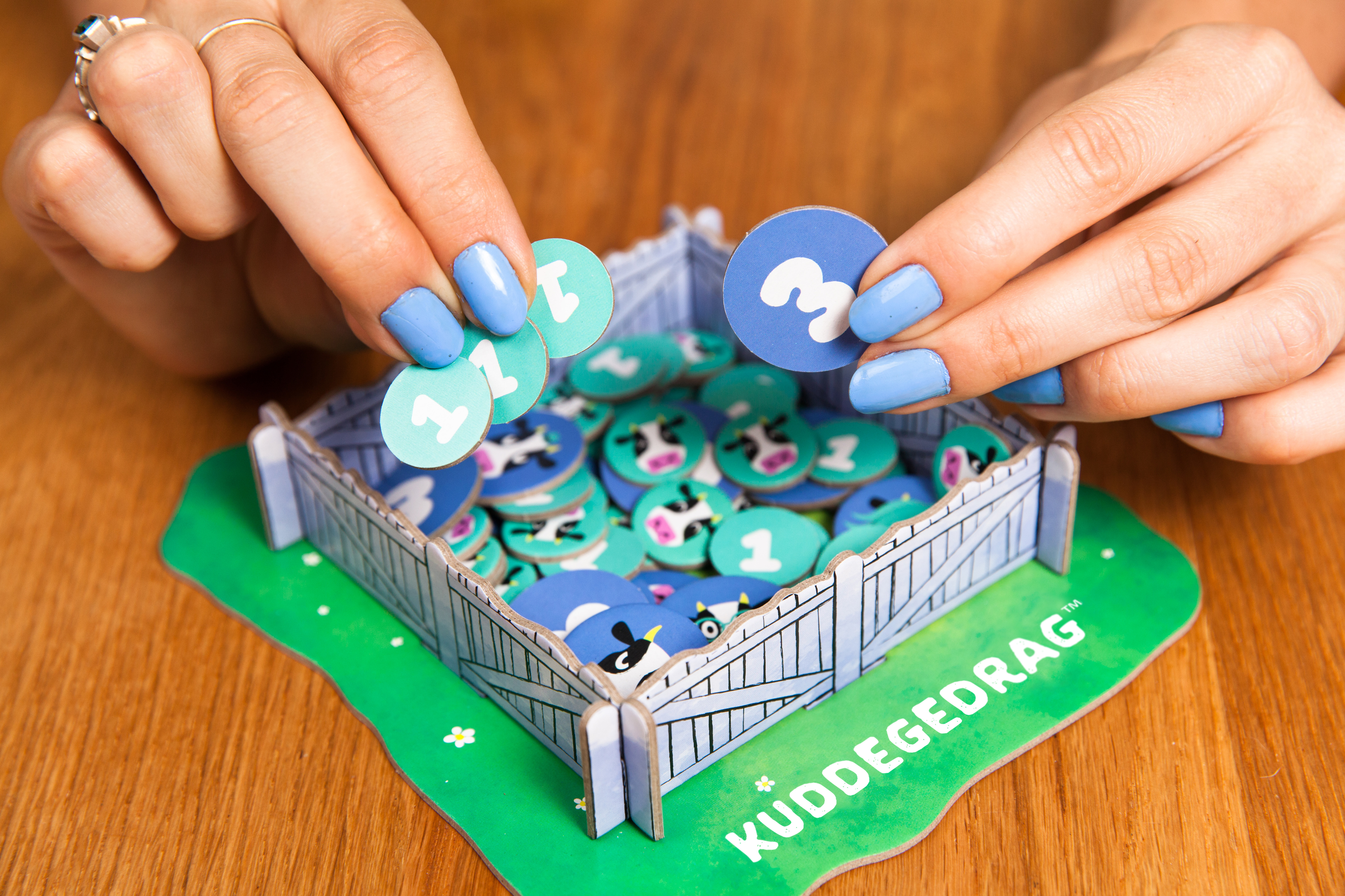 Hände spielen ein Spiel mit Kühen-Themen-Spielsteinen und einem zaunartigen Spielbrett.