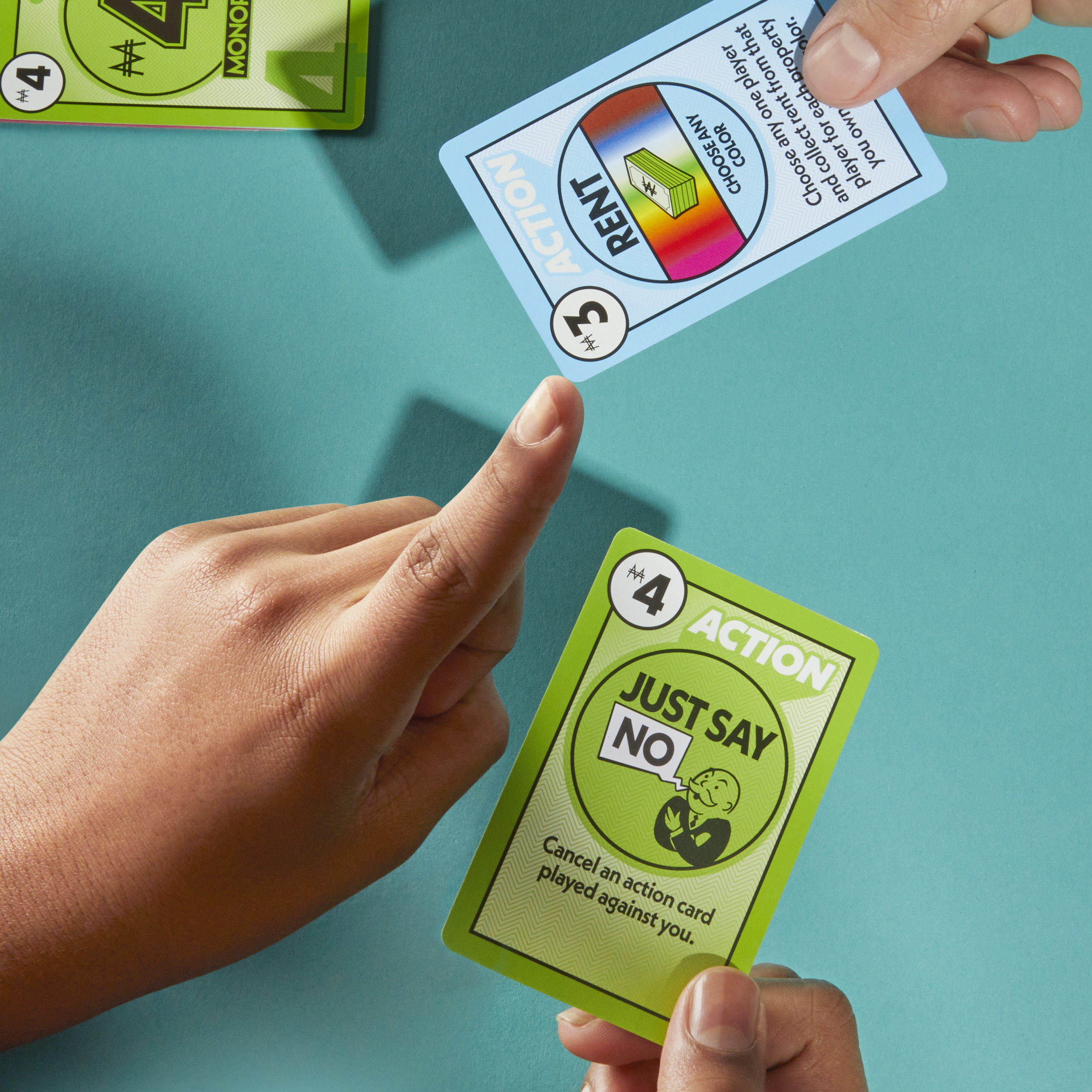 Ręce grające w karty Monopoly. Jedna ręka ma zamiar położyć kartę.