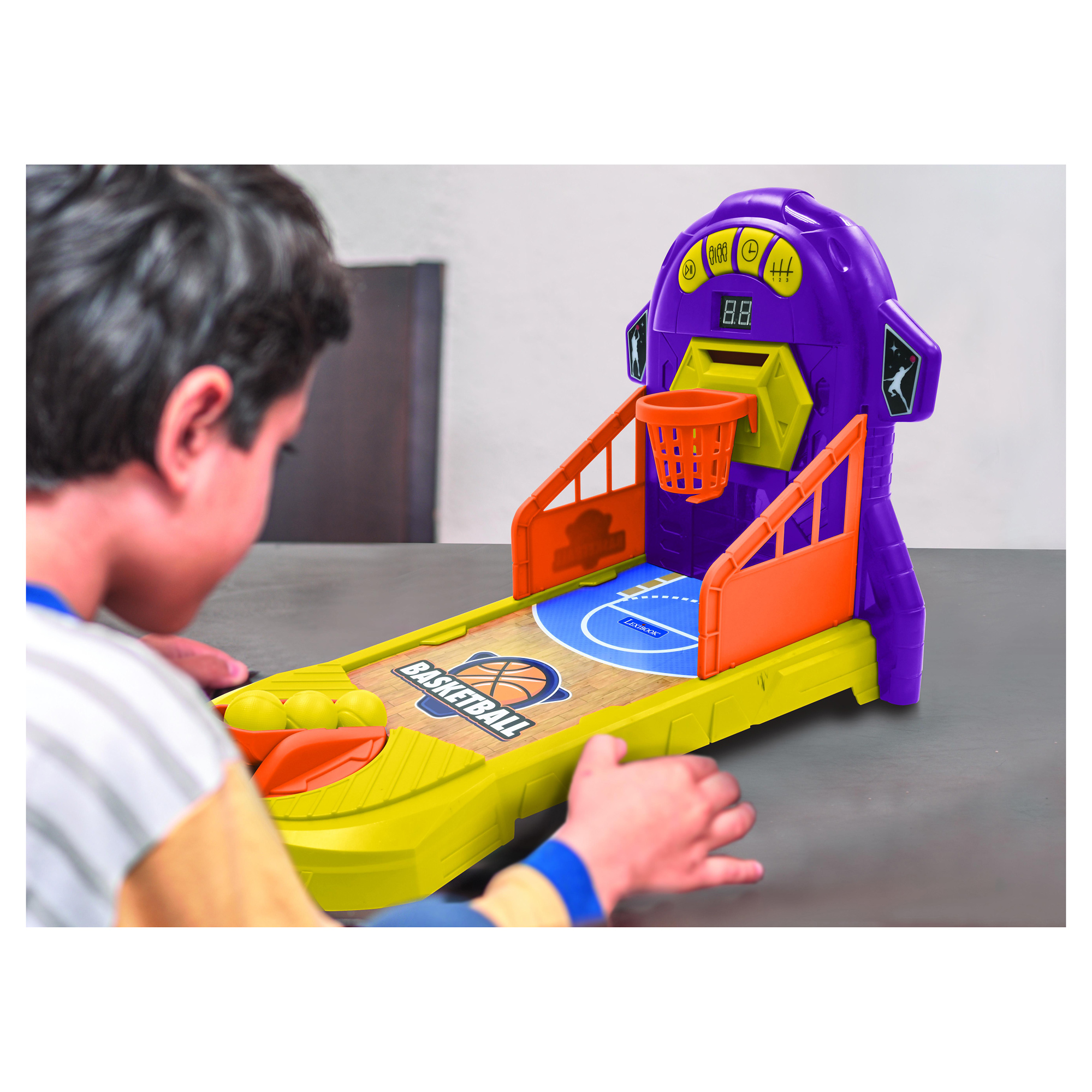 Ragazzo che gioca a un gioco arcade di basket. Il gioco è viola, arancione e giallo. Tavolo grigio.