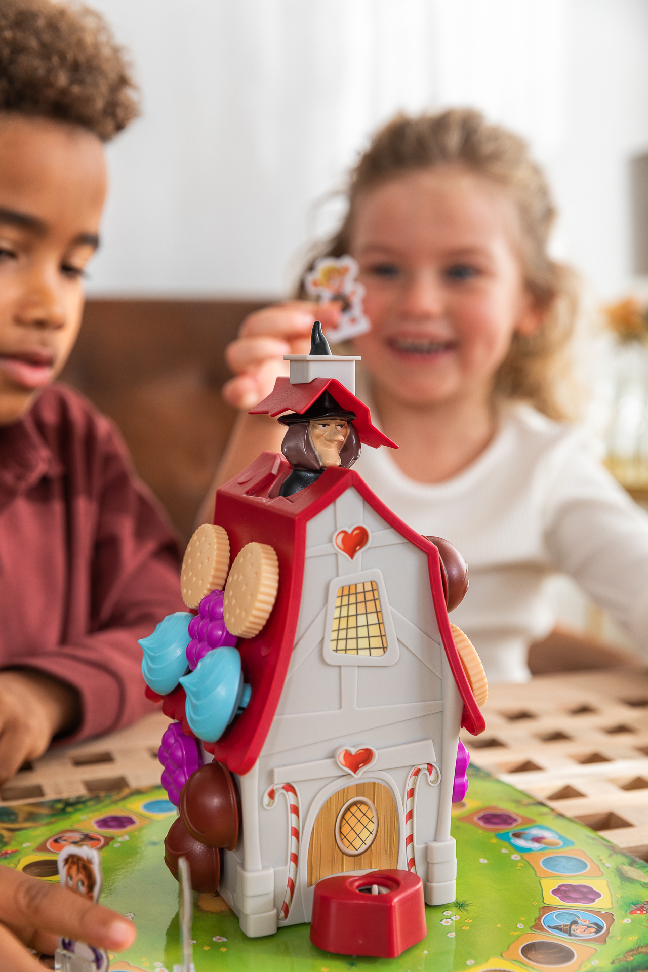 Kinderen spelen een bordspel met een huis met heksenthema. Het huis heeft snoep en versieringen.