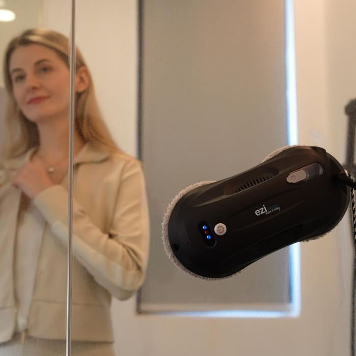 Kobieta przegląda się w lustrze. Robot do czyszczenia okien jest na lustrze.