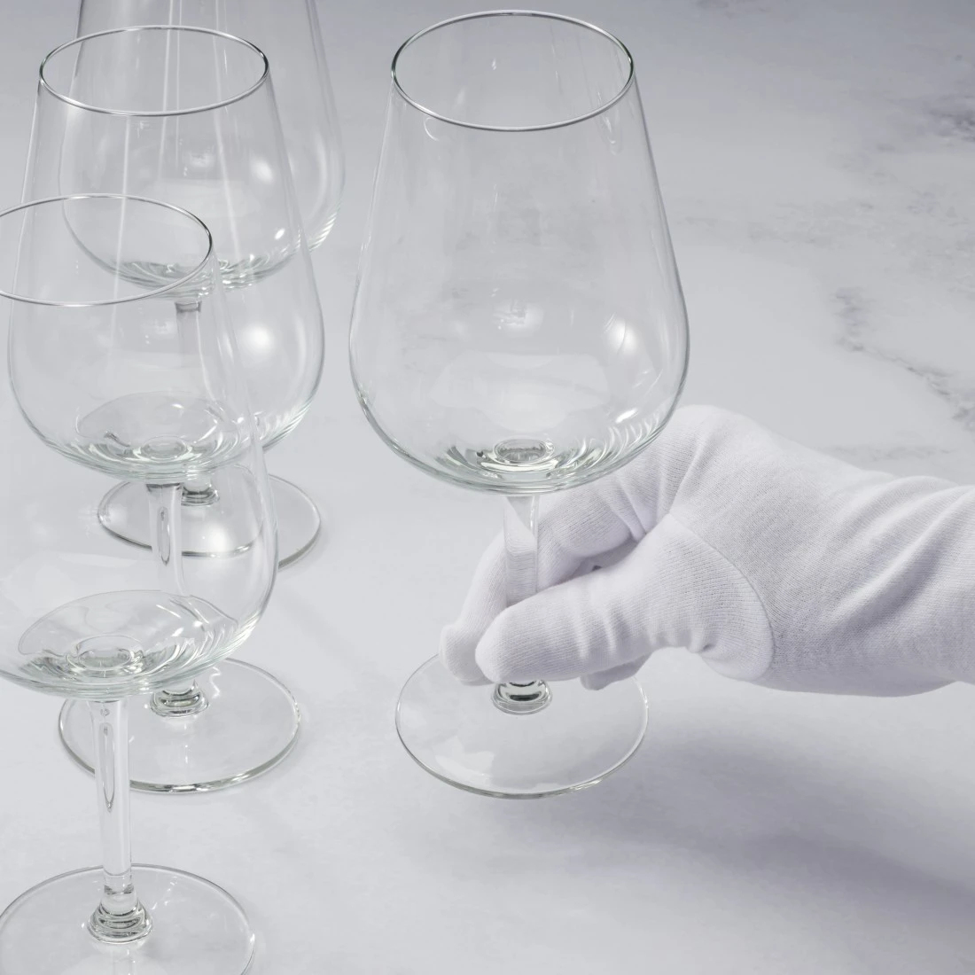 Una mano con un guanto bianco tiene un bicchiere di vino, con altri bicchieri sullo sfondo.