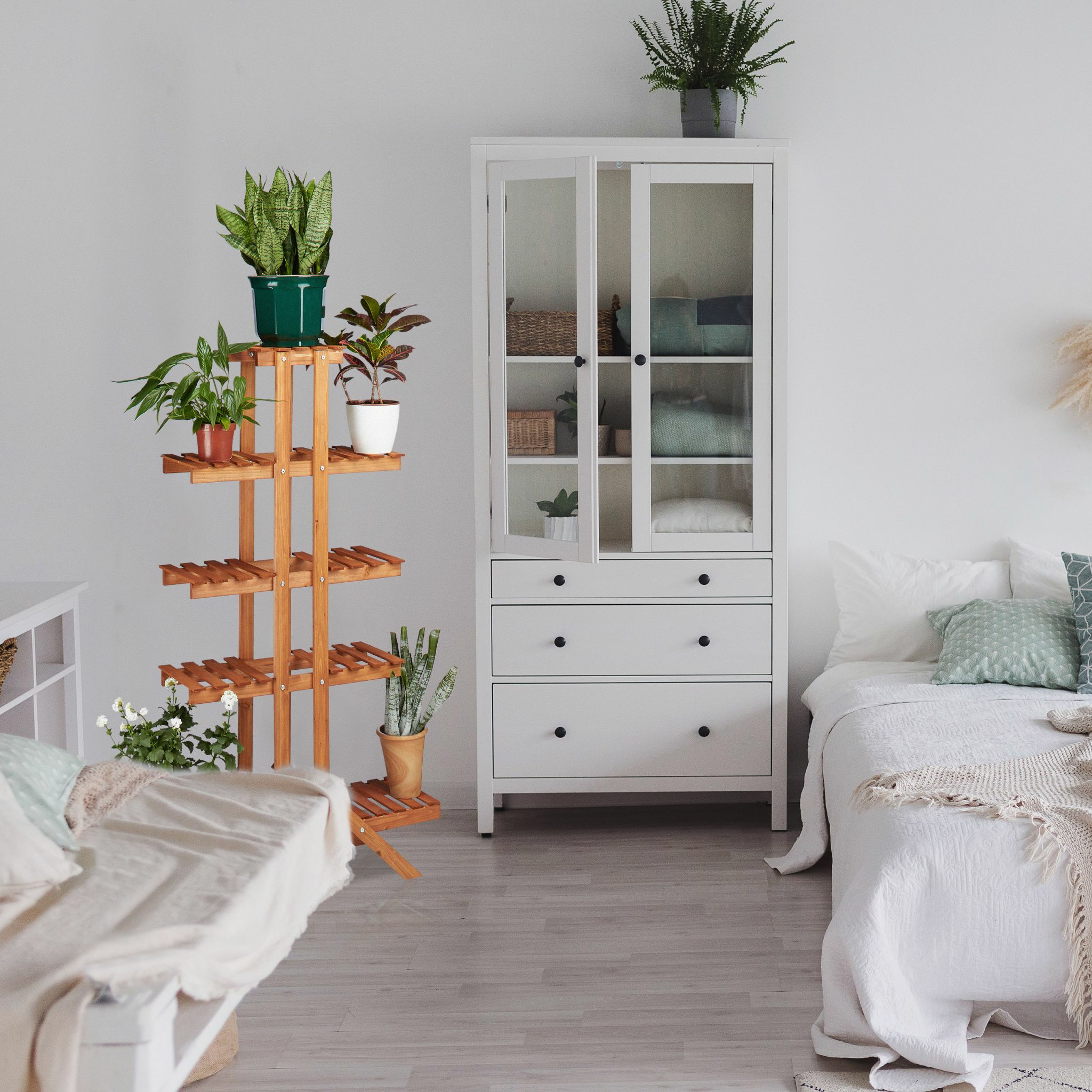 Ein Wohnzimmer mit einem hölzernen Pflanzenständer und einem weißen Schrank mit Glastüren. Pflanzen und ein Bett sind sichtbar.