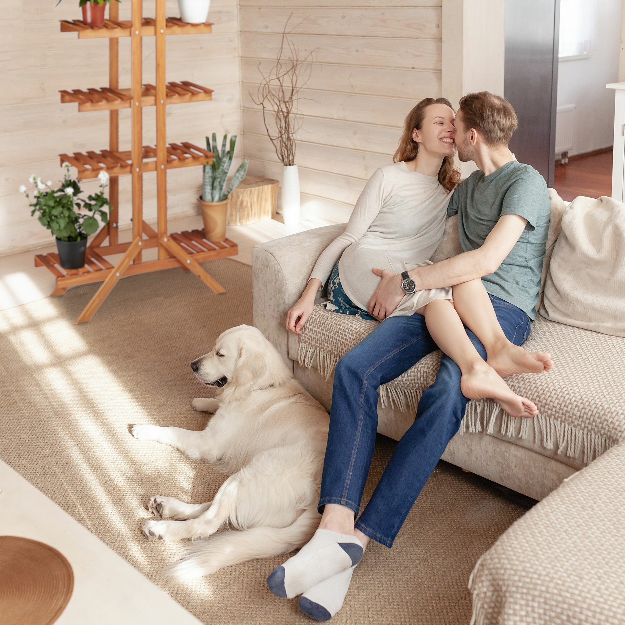 Paar küsst sich auf beigem Sofa mit Hund. Pflanzenständer aus Holz links.