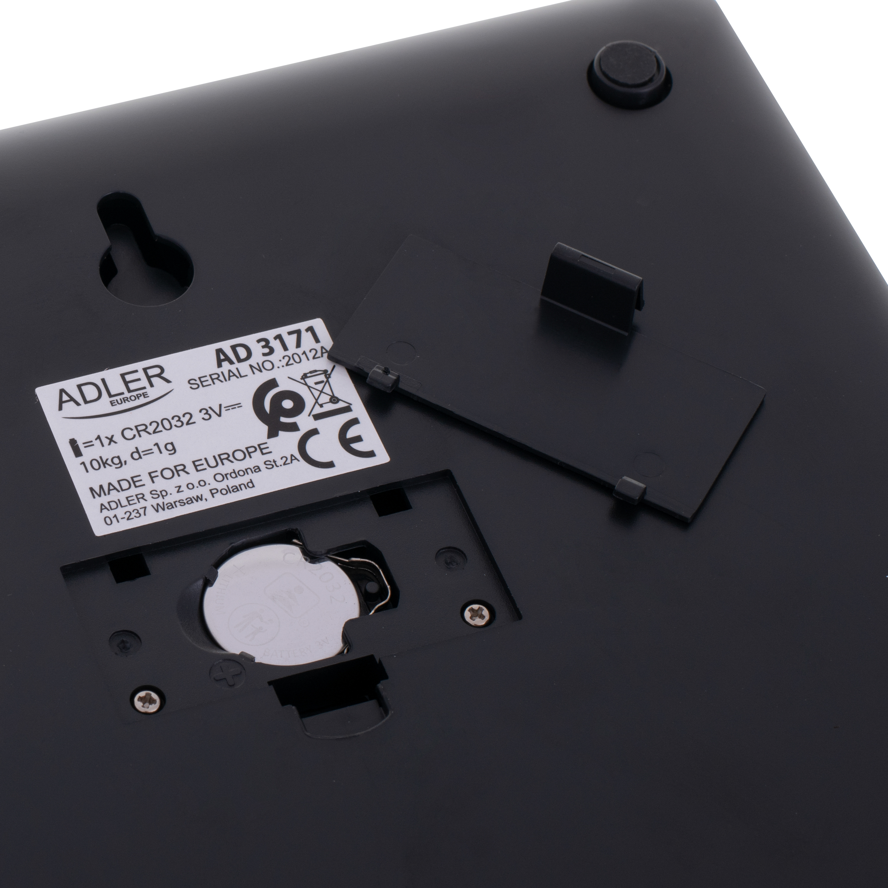 Spód wagi cyfrowej. Pokazuje komorę baterii i etykiety z informacjami o produkcie.