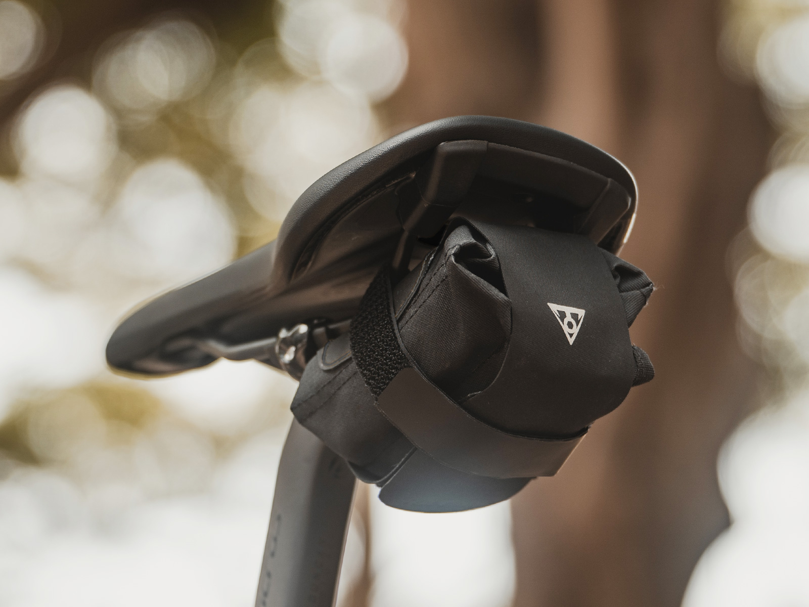 Czarna torba na siodełko rowerowe przymocowana do siodełka, z białym logo.