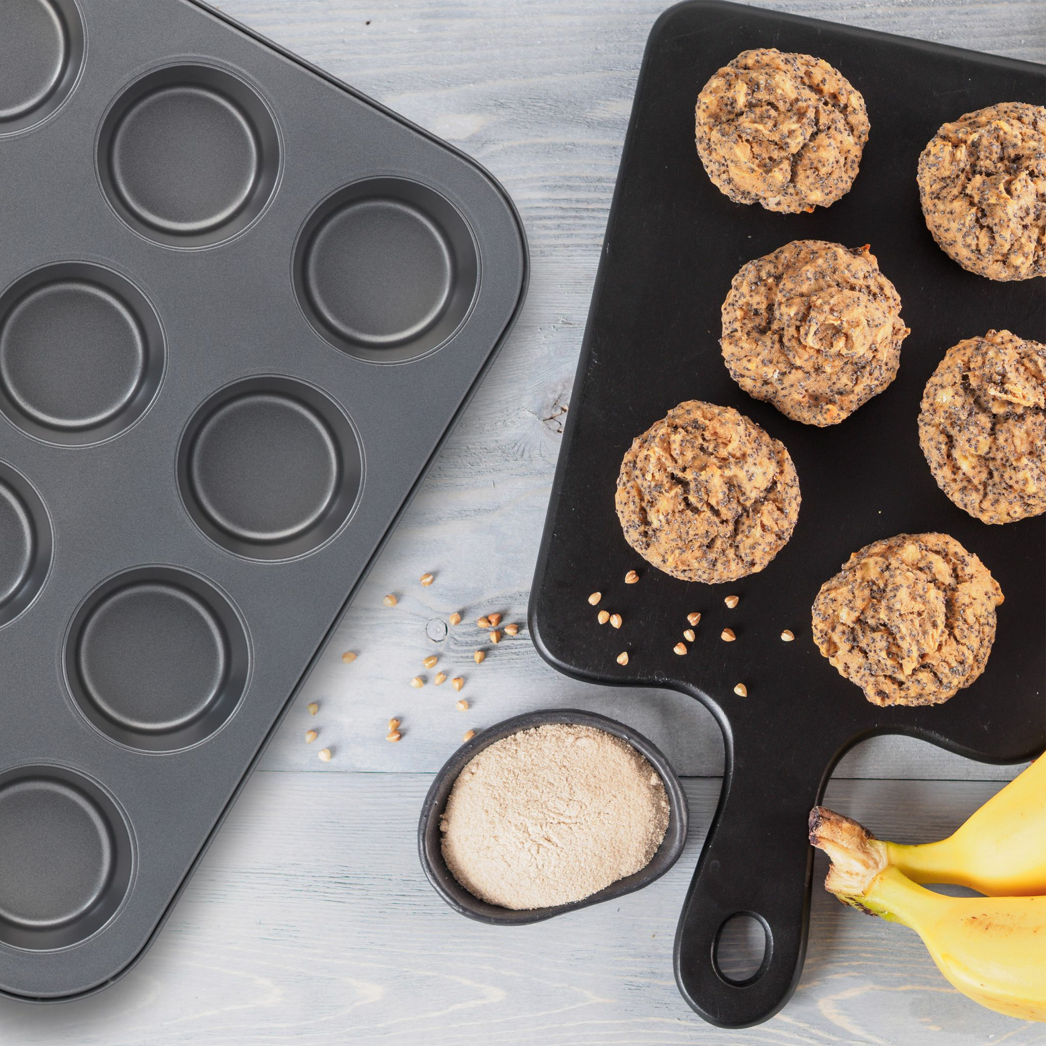 Muffinform, Muffins, Schüssel mit Mehl und Bananen auf einer hellgrauen Holzoberfläche.