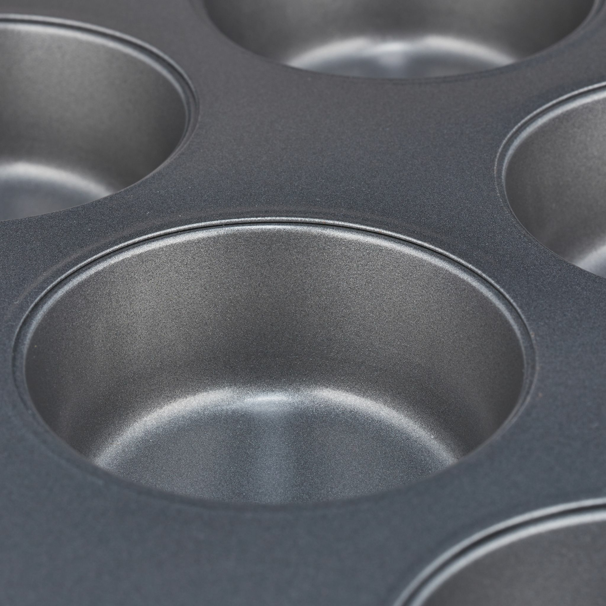 Nahaufnahme einer grauen Metall-Muffinform. Die Formen sind sichtbar. Weißer Hintergrund.