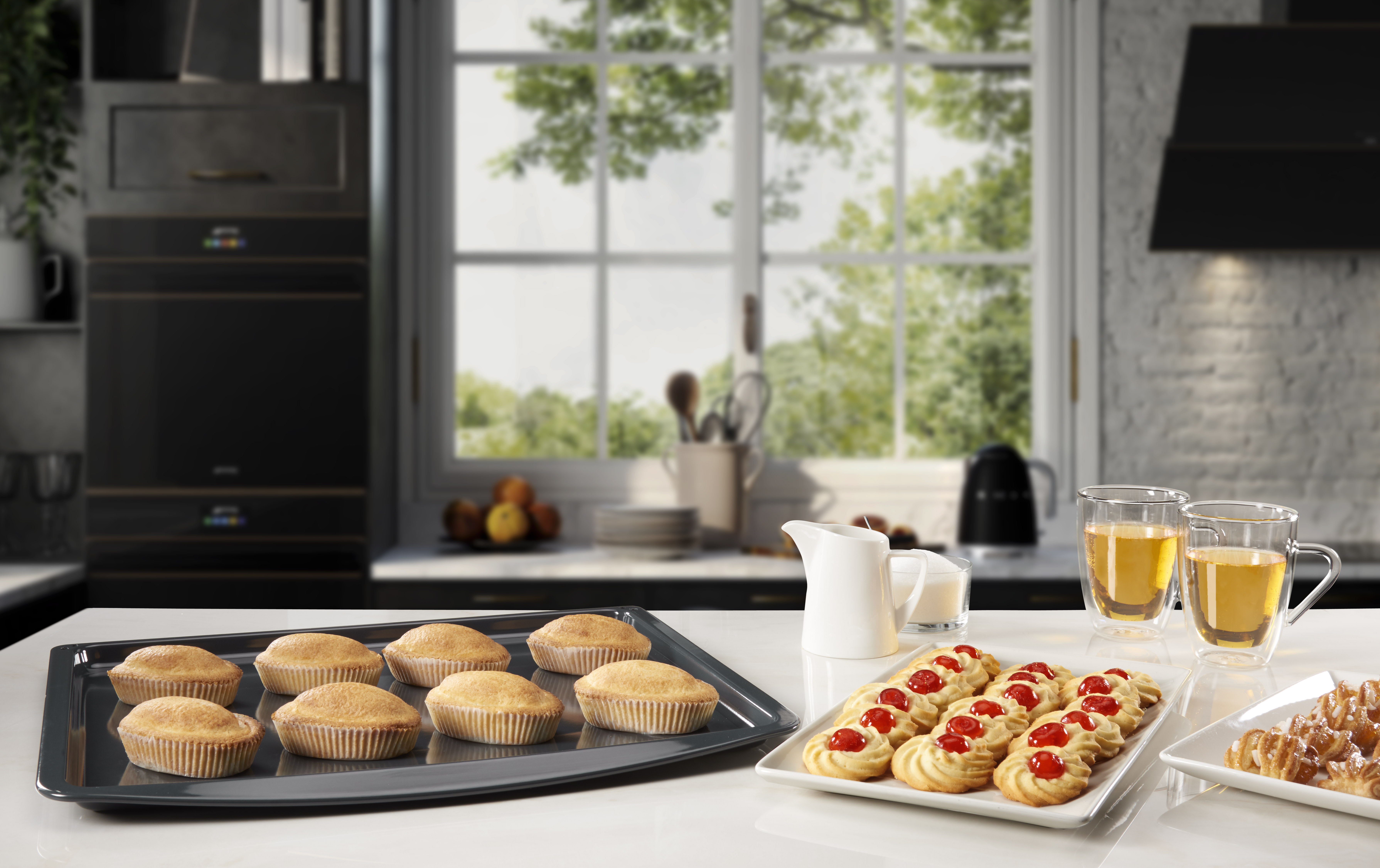 Escena de cocina con productos horneados en bandeja y platos. Encimera blanca, armarios oscuros y ventana al fondo.
