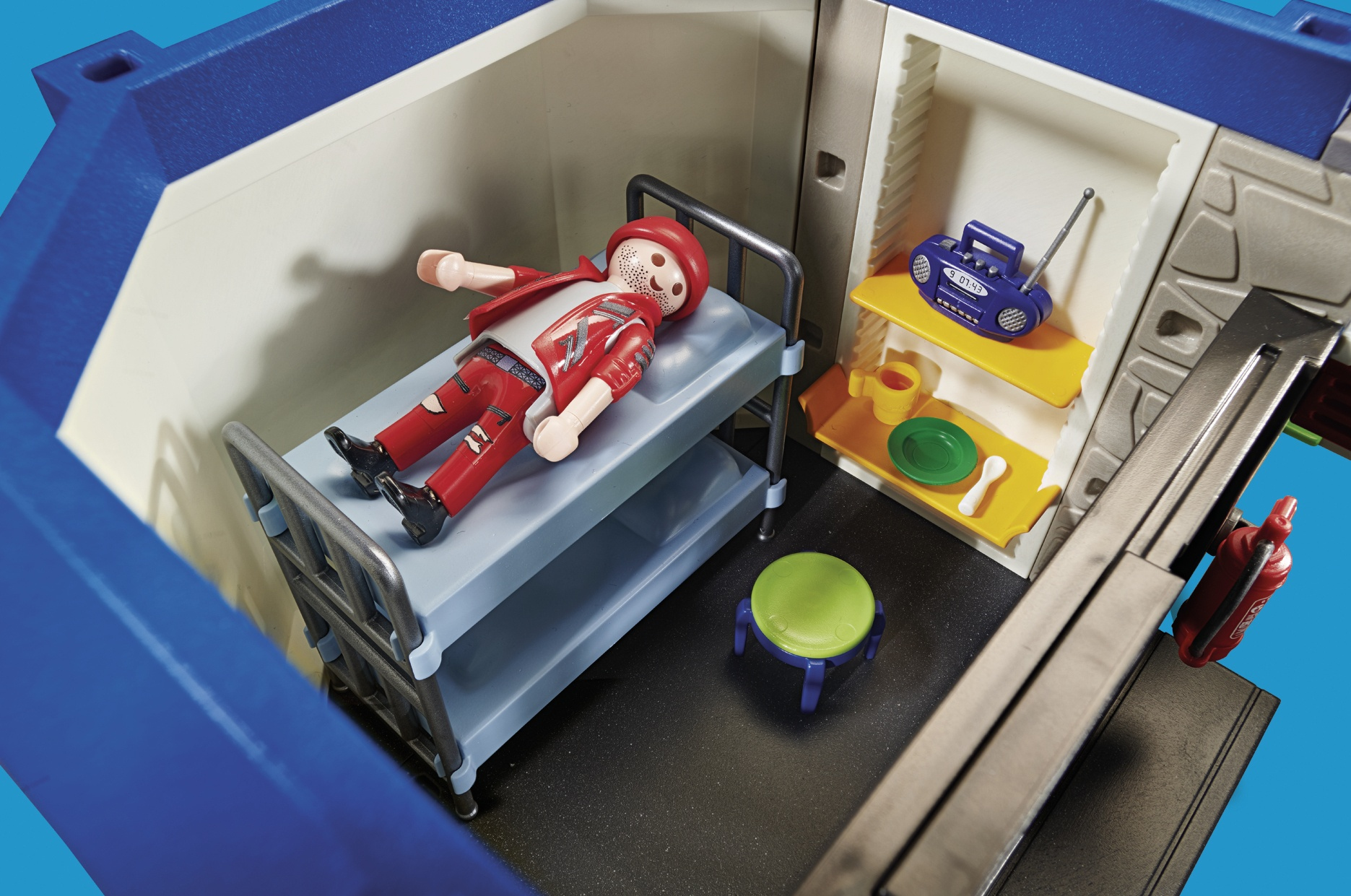 Scena Playmobil: ranna postać na łóżku, półki z przedmiotami, niebieski pokój.