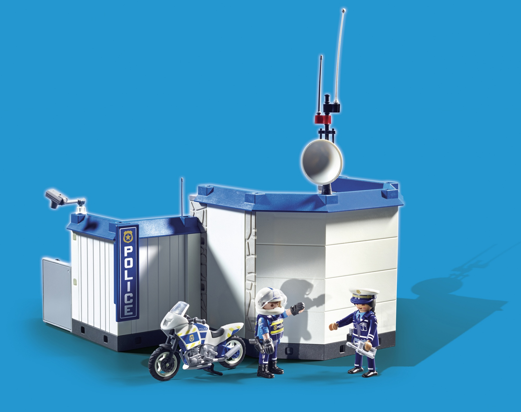 Posterunek policji Playmobil z figurkami i motocyklem. Niebieskie tło.