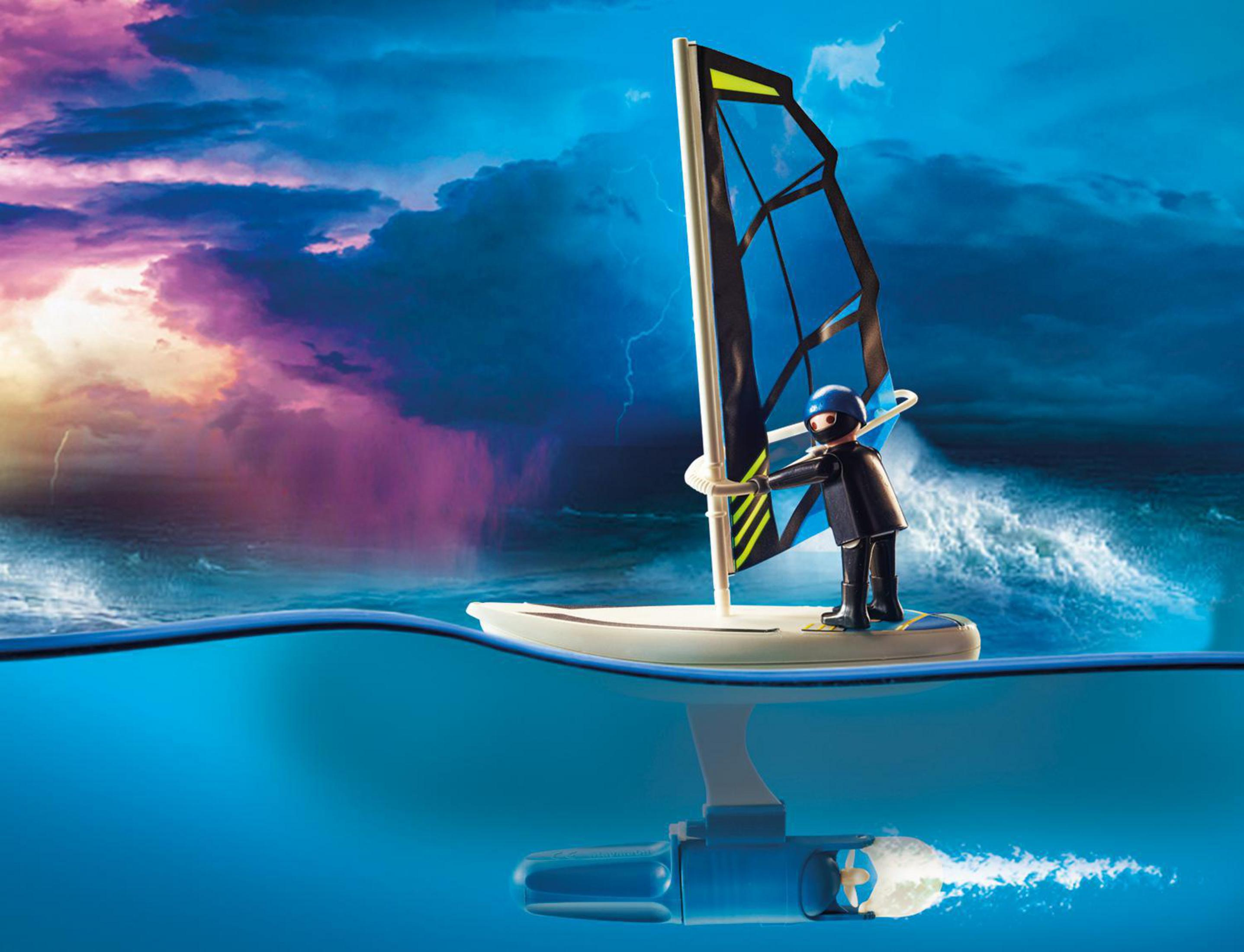 Windsurfista Playmobil en el agua. Cielo tormentoso de fondo. Figura en tabla, vela azul. Reflejo del agua.