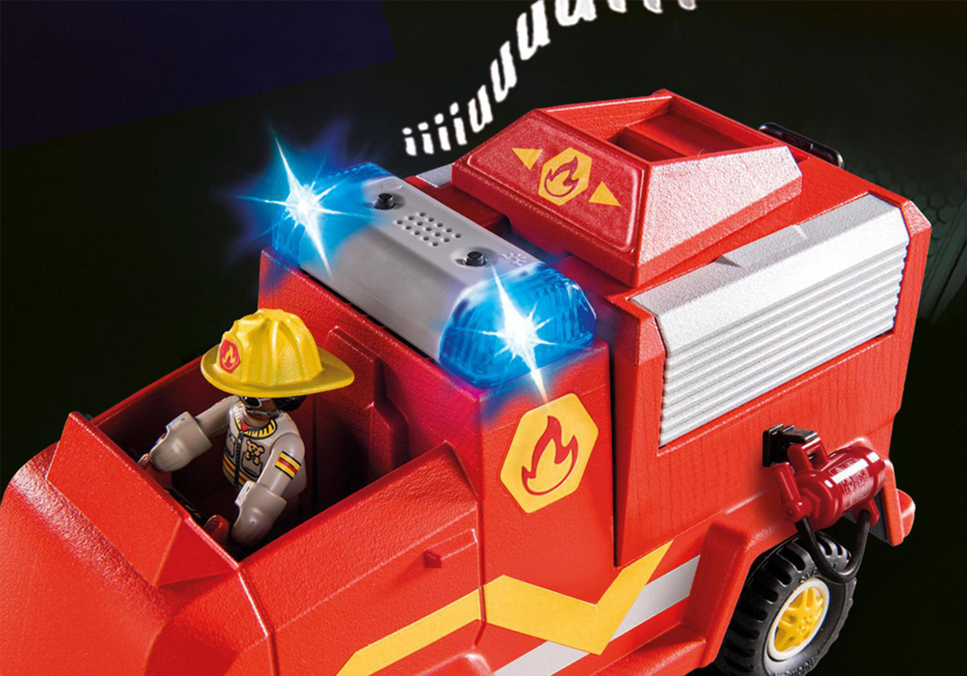 Ein Playmobil-Feuerwehrwagen mit eingeschaltetem Licht. Ein Feuerwehrmann sitzt am Steuer. Der Hintergrund ist dunkel.