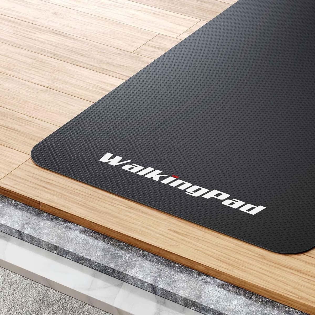 Tappetino WalkingPad nero su pavimento in legno, con il logo bianco. Il tappetino è su pavimento in legno e cemento.