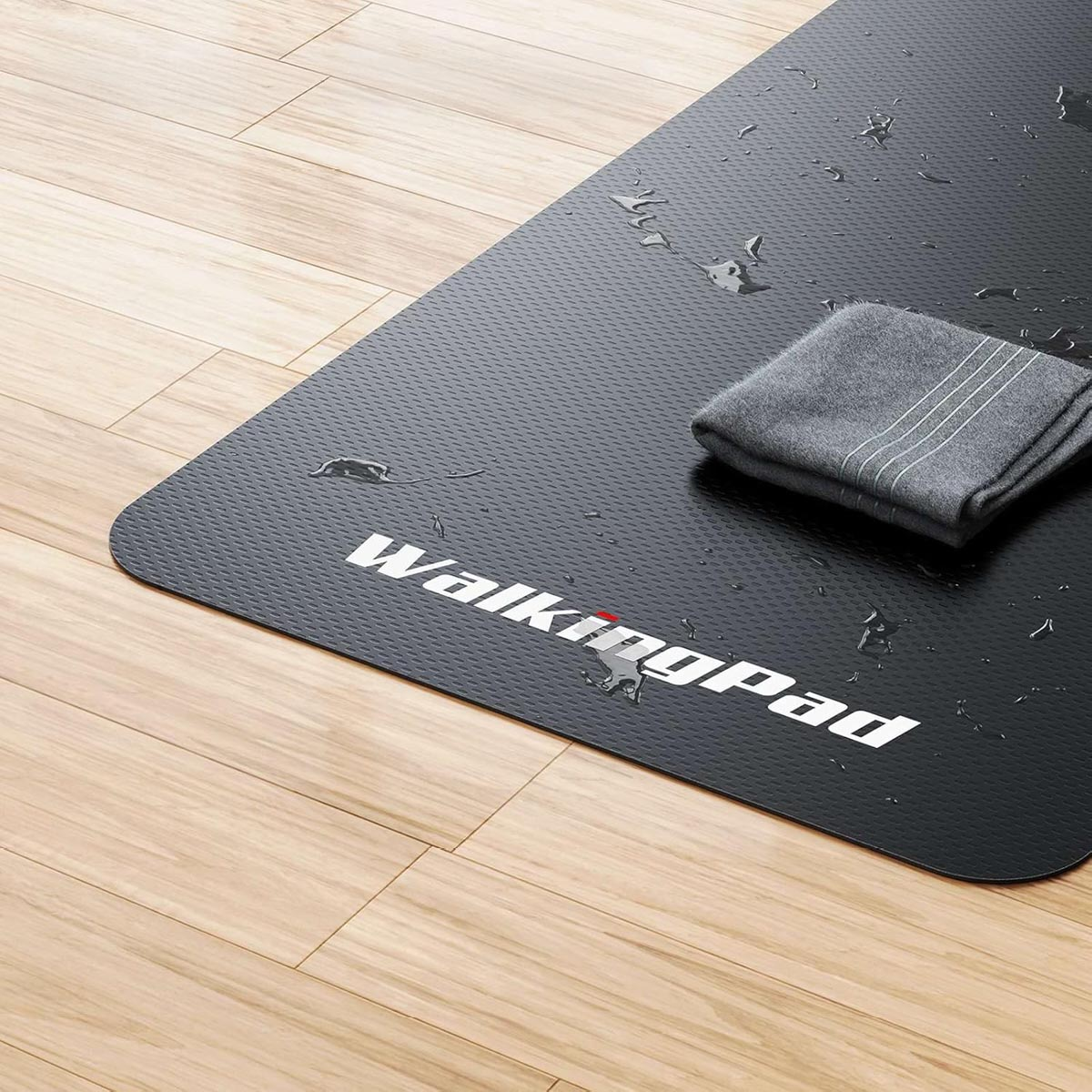 Un tappeto da camminata nero con gocce d'acqua e un asciugamano grigio. Il marchio 'WalkingPad' è visibile.