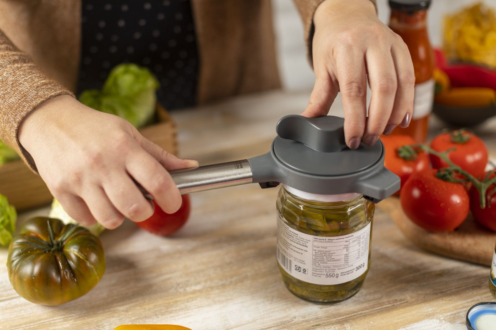 Mani di una persona che usa un apriscatole su un barattolo di pesto, circondato da verdure.