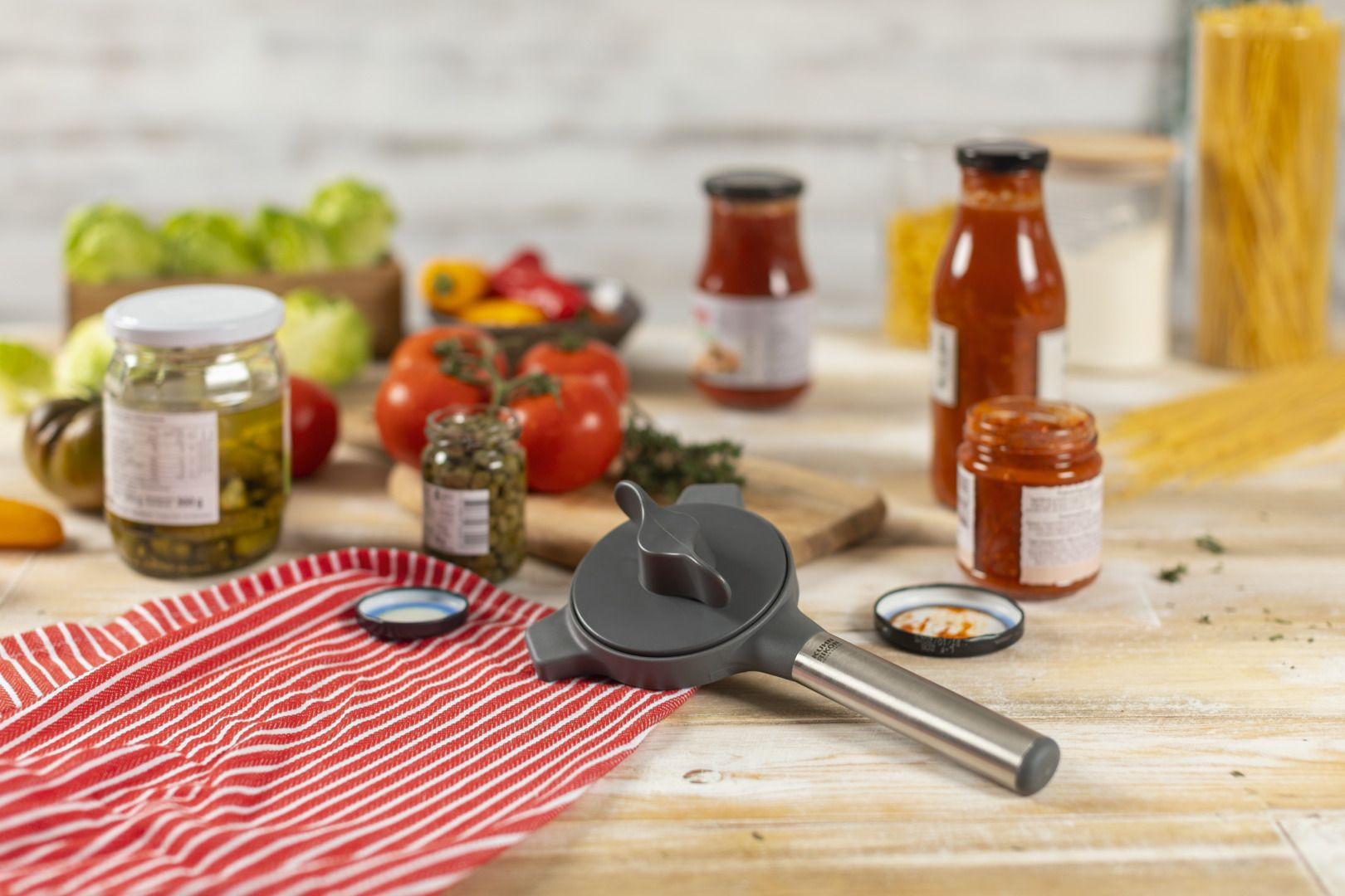 Una scena di cucina con un apriscatole, barattoli, pomodori e pasta, su una superficie di legno.