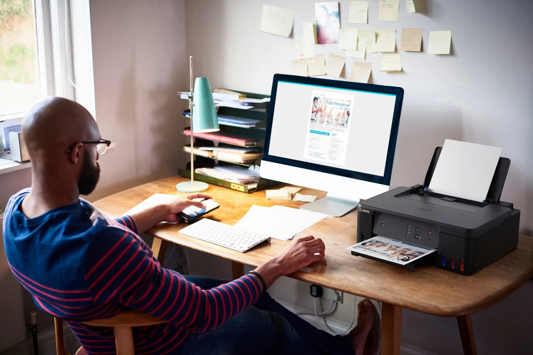 Mężczyzna siedzący przy biurku z drukarką i komputerem, pracujący. Białe tło.
