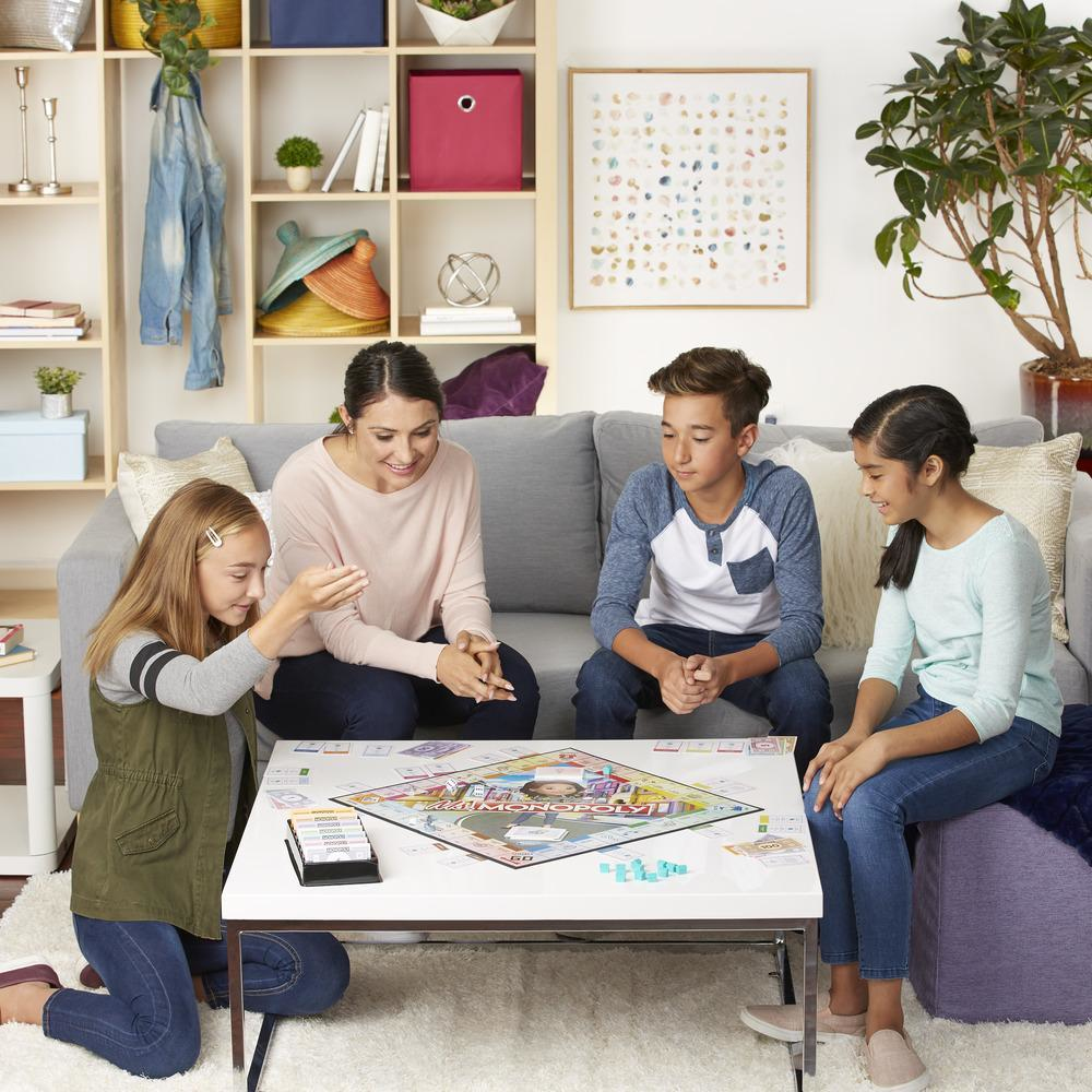 Familie spielt Monopoly. Eine Frau und drei Kinder sitzen um einen Tisch.