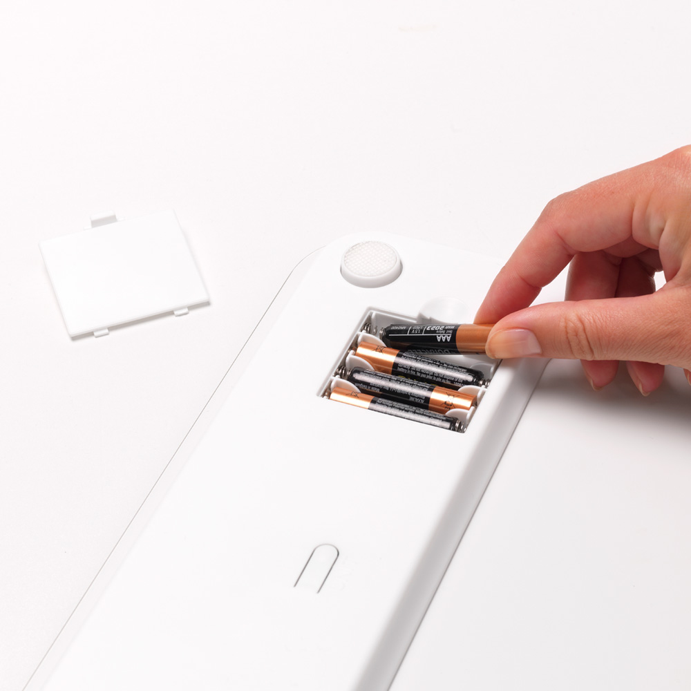 Eine Hand legt eine AAA-Batterie in eine weiße Waage ein. Weißer Hintergrund.