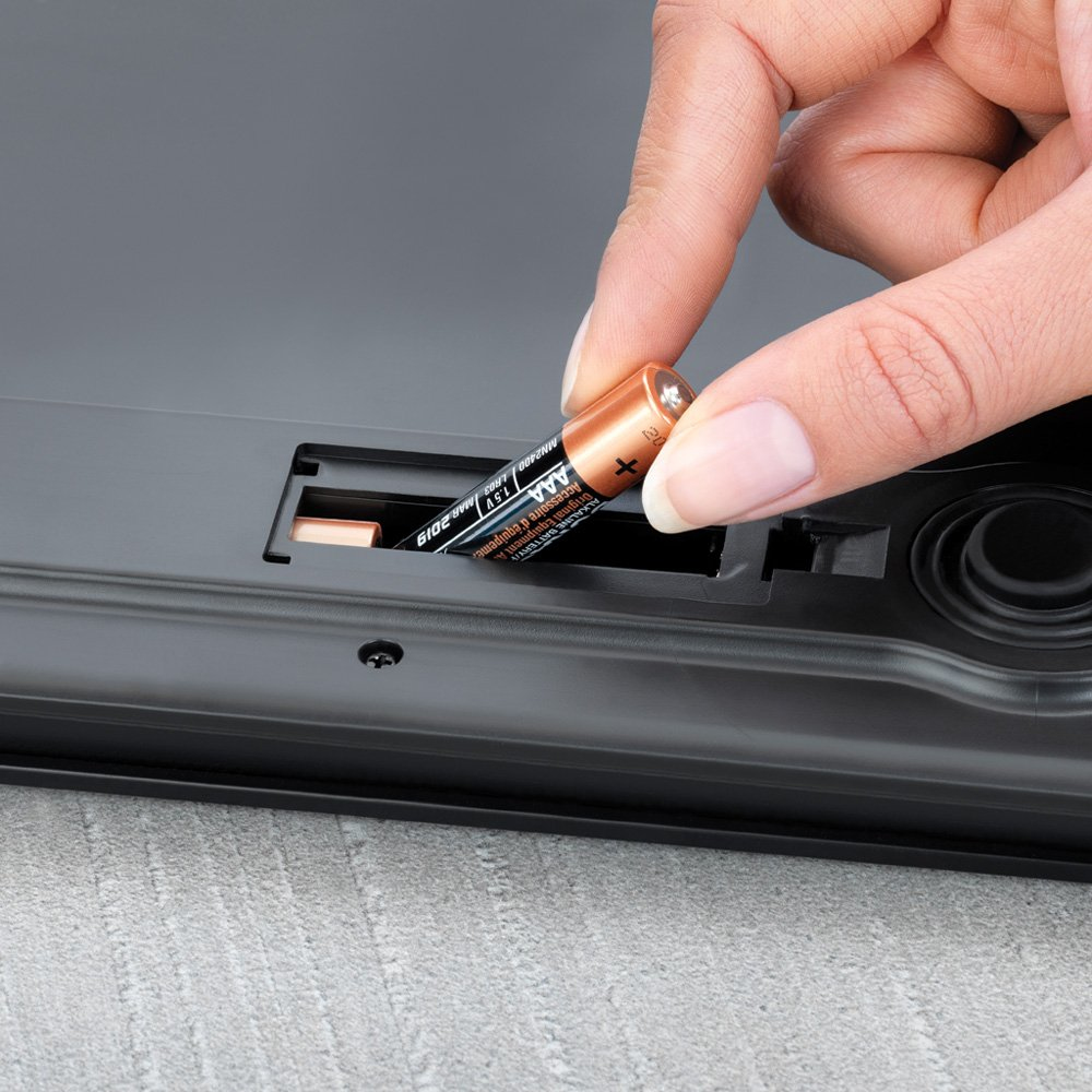 Dłoń wkładająca baterię do komory w czarnej wadze. Zbliżenie.