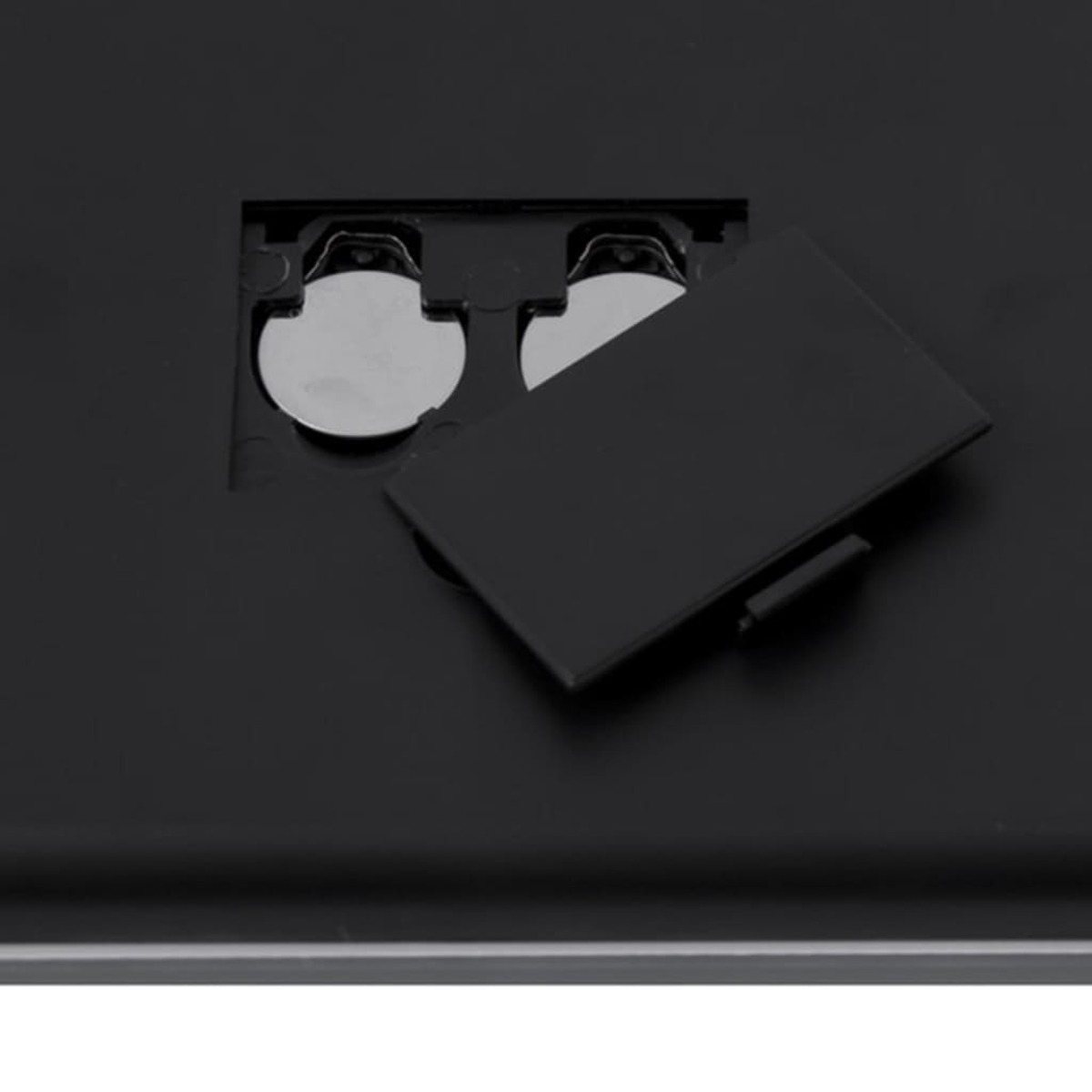 Primo piano di un vano batterie con due batterie a bottone e il coperchio nero aperto.