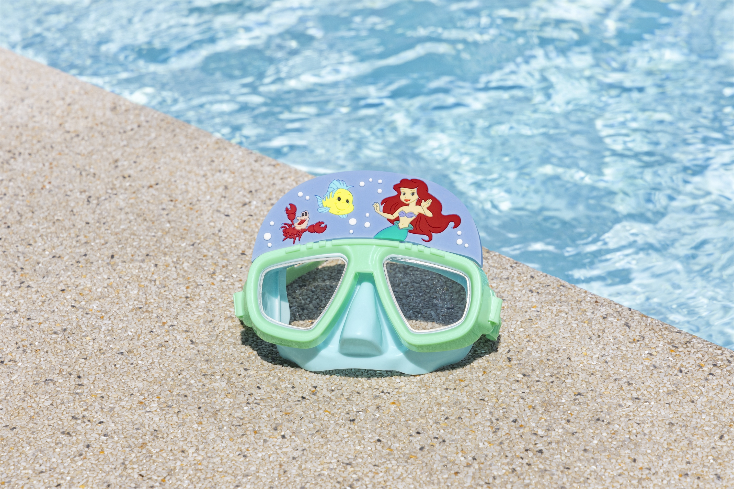 Una maschera subacquea a tema La Sirenetta. È sul bordo di una piscina. Acqua limpida.