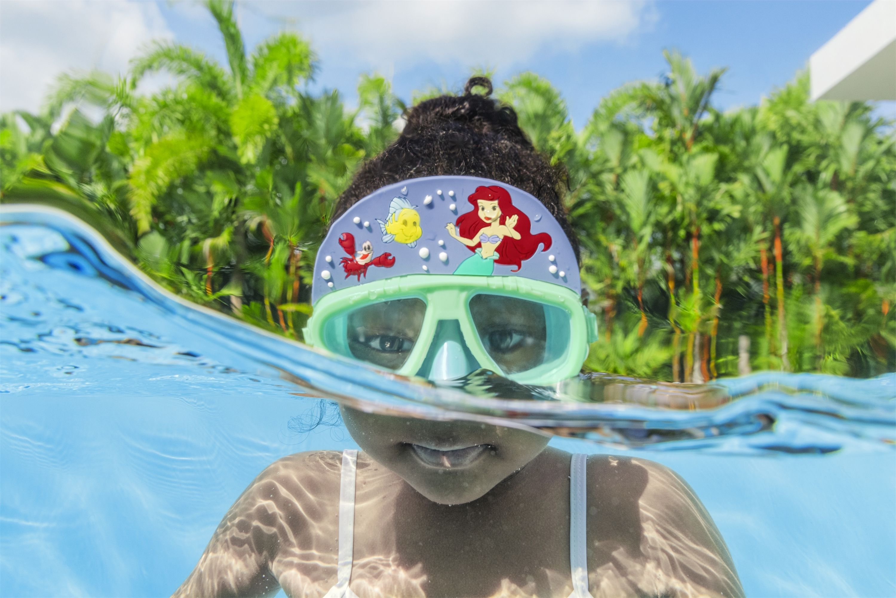 Una ragazza con una maschera de La Sirenetta in piscina, sopra e sotto l'acqua.