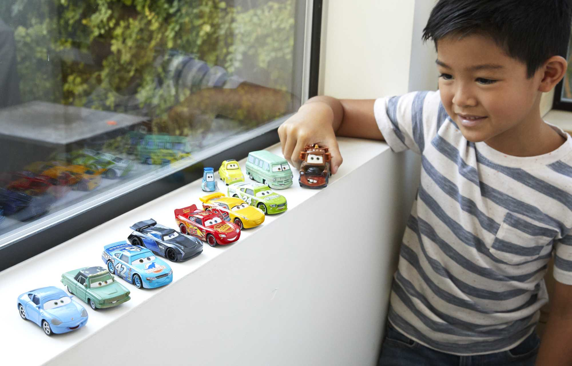 Ein Junge mit Spielzeugautos auf einer Fensterbank.