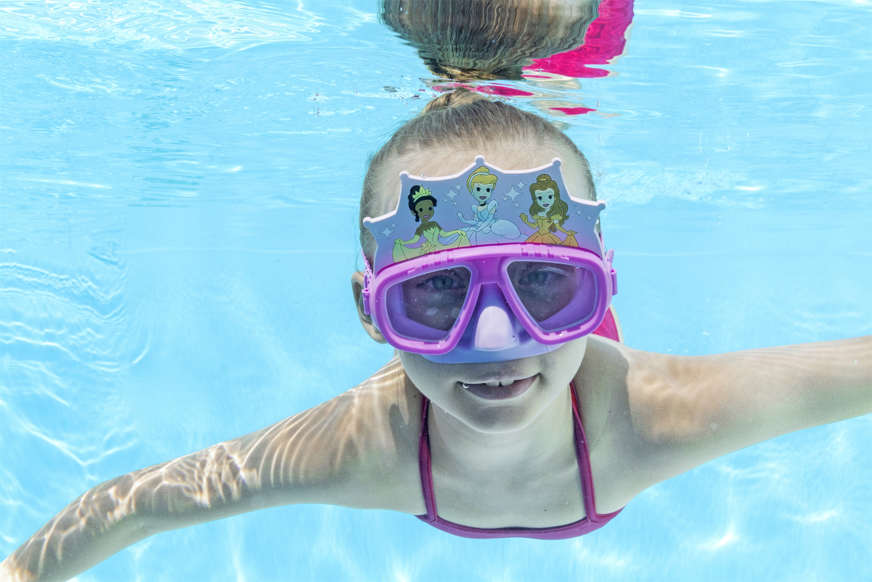 Una bambina sott'acqua in una piscina, con occhiali da principessa.