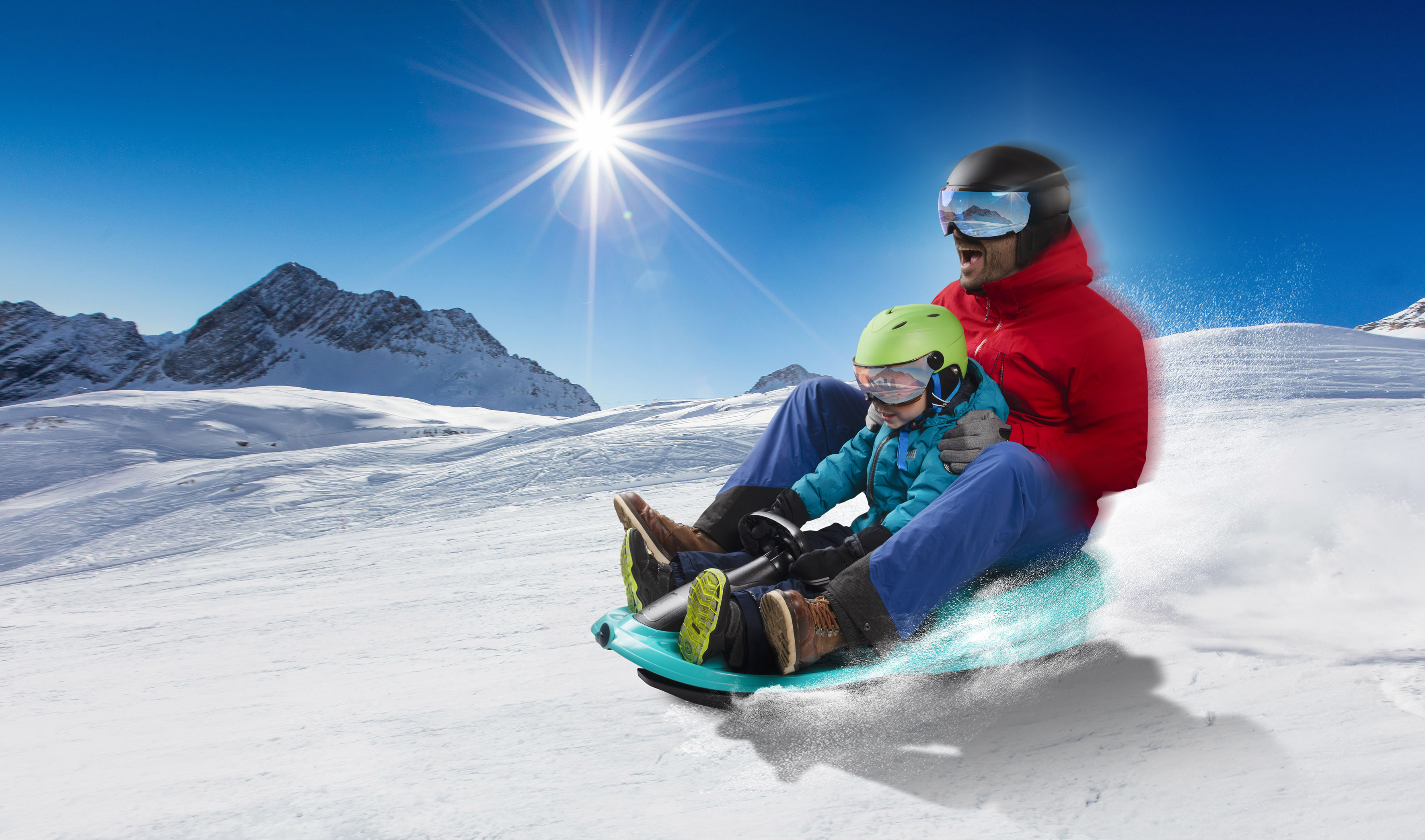Padre e figlio che vanno in slitta su un pendio innevato sotto il sole splendente e il cielo blu.