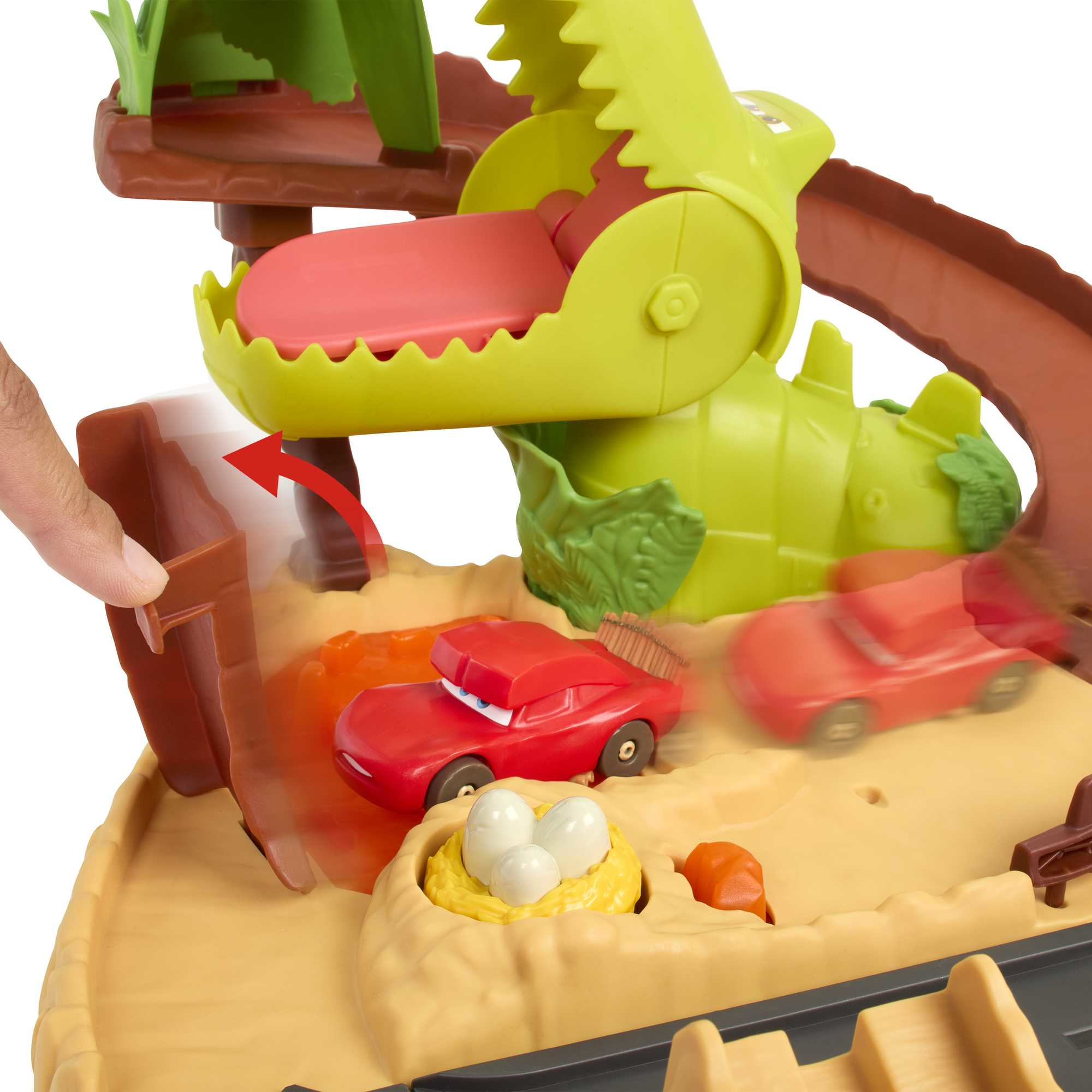 Spielzeug-Dinosaurier mit roten Autos. Eines ist in seinem Maul, eines fällt in eine Lava-Grube.