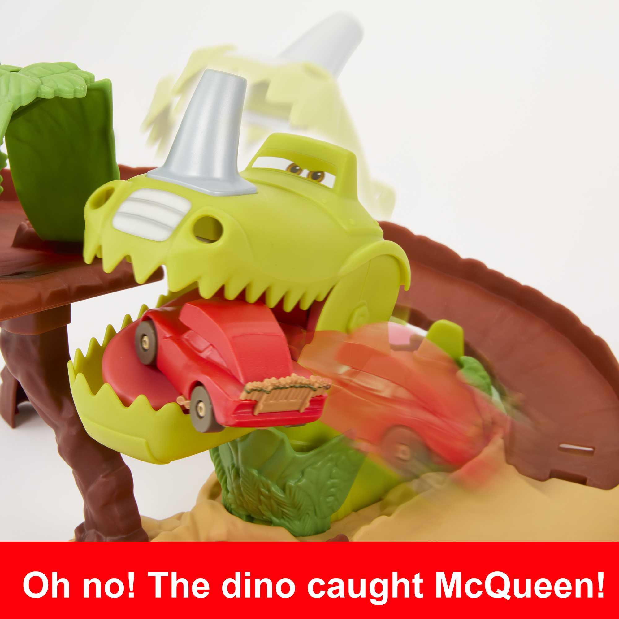 Ein rotes Auto wird von einem grünen Dinosaurierspielzeug gefangen. Text: Oh nein! Der Dino erwischte McQueen.