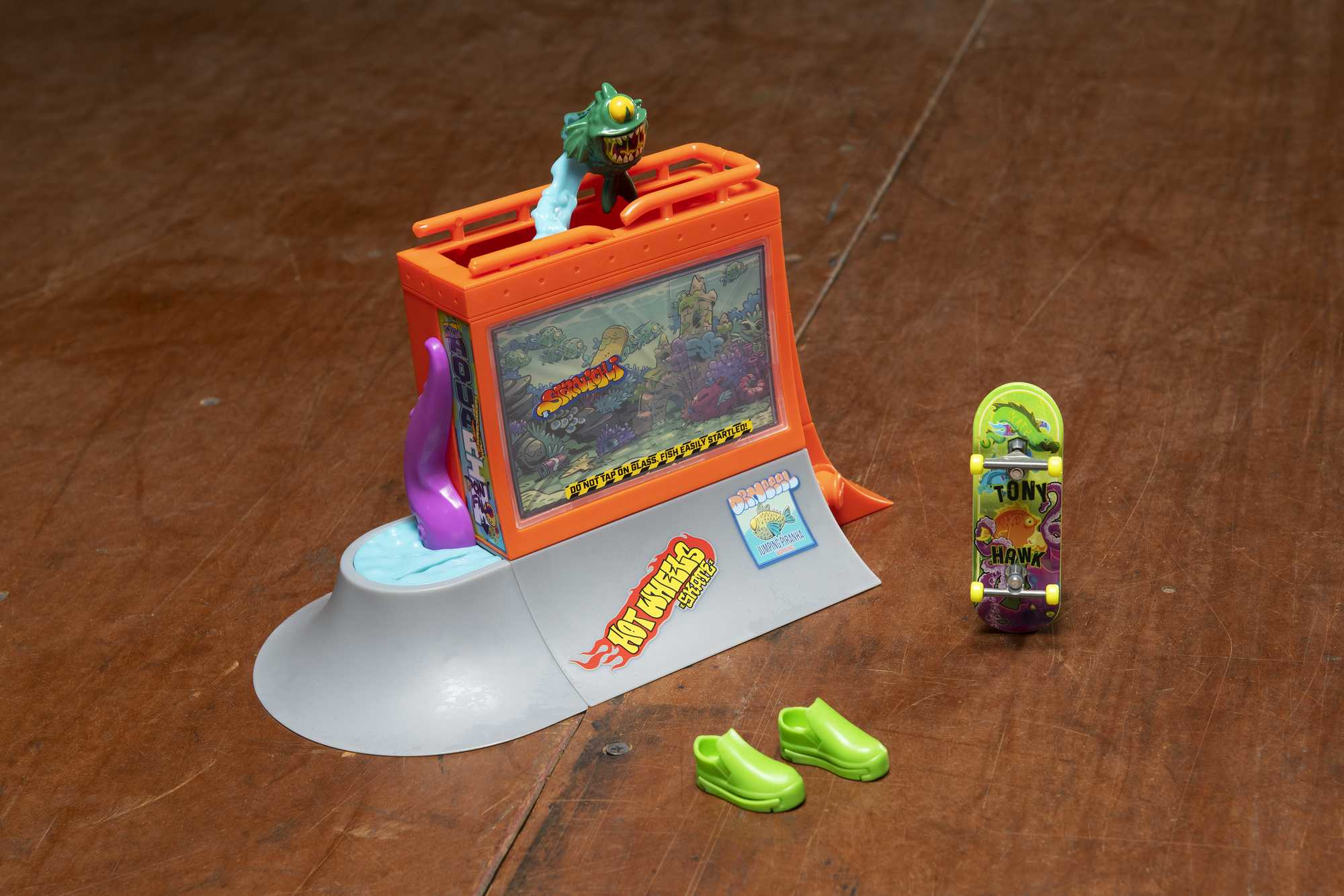 Pomarańczowy zestaw zabawek z akwarium, deskorolką, butami i figurką stworzenia.