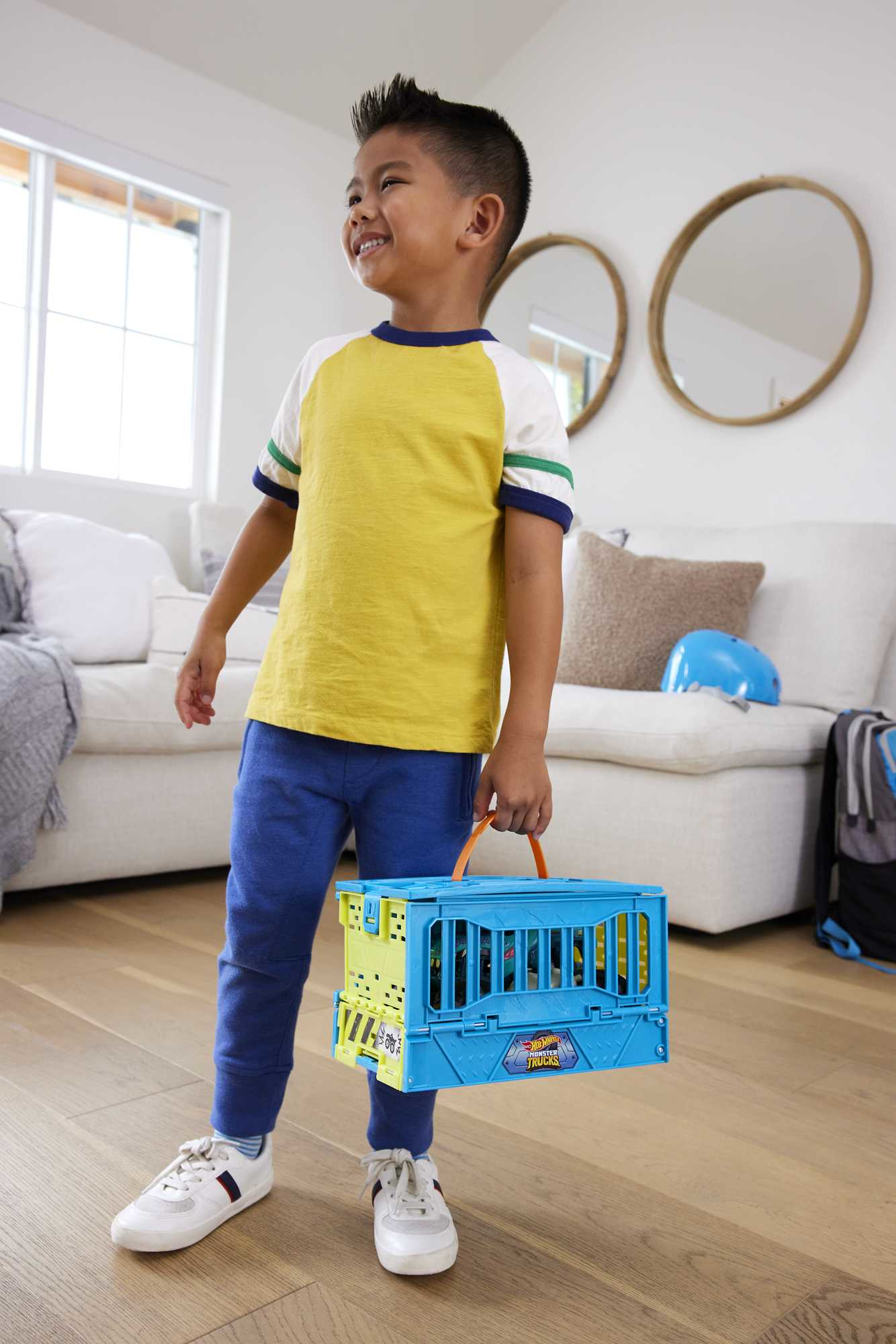 Junge hält einen blau-orangenen Dinosaurier-Spielzeugkäfig im Wohnzimmer, lächelnd.
