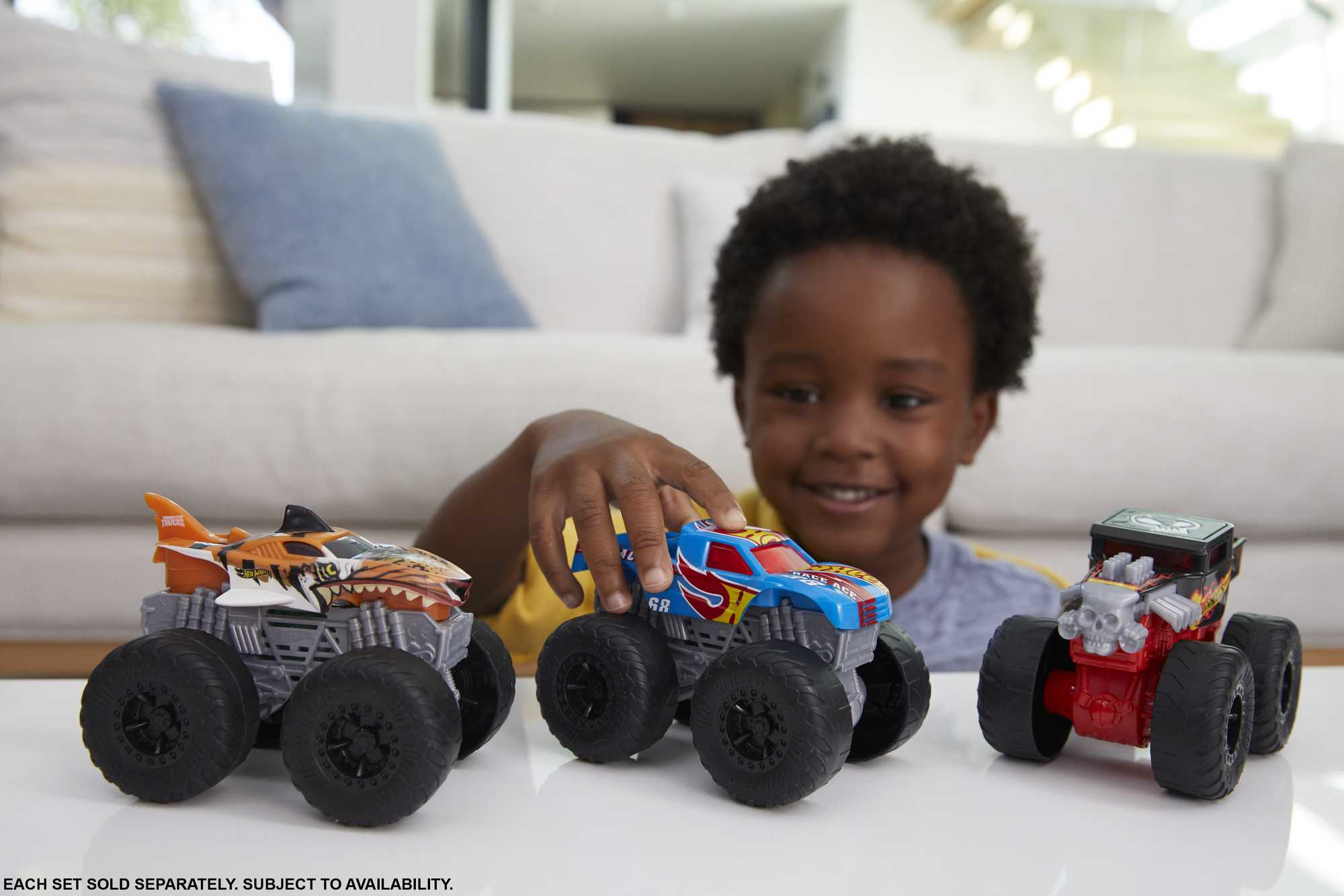 Ein junger Junge spielt mit drei Monstertrucks auf einer weißen Oberfläche.