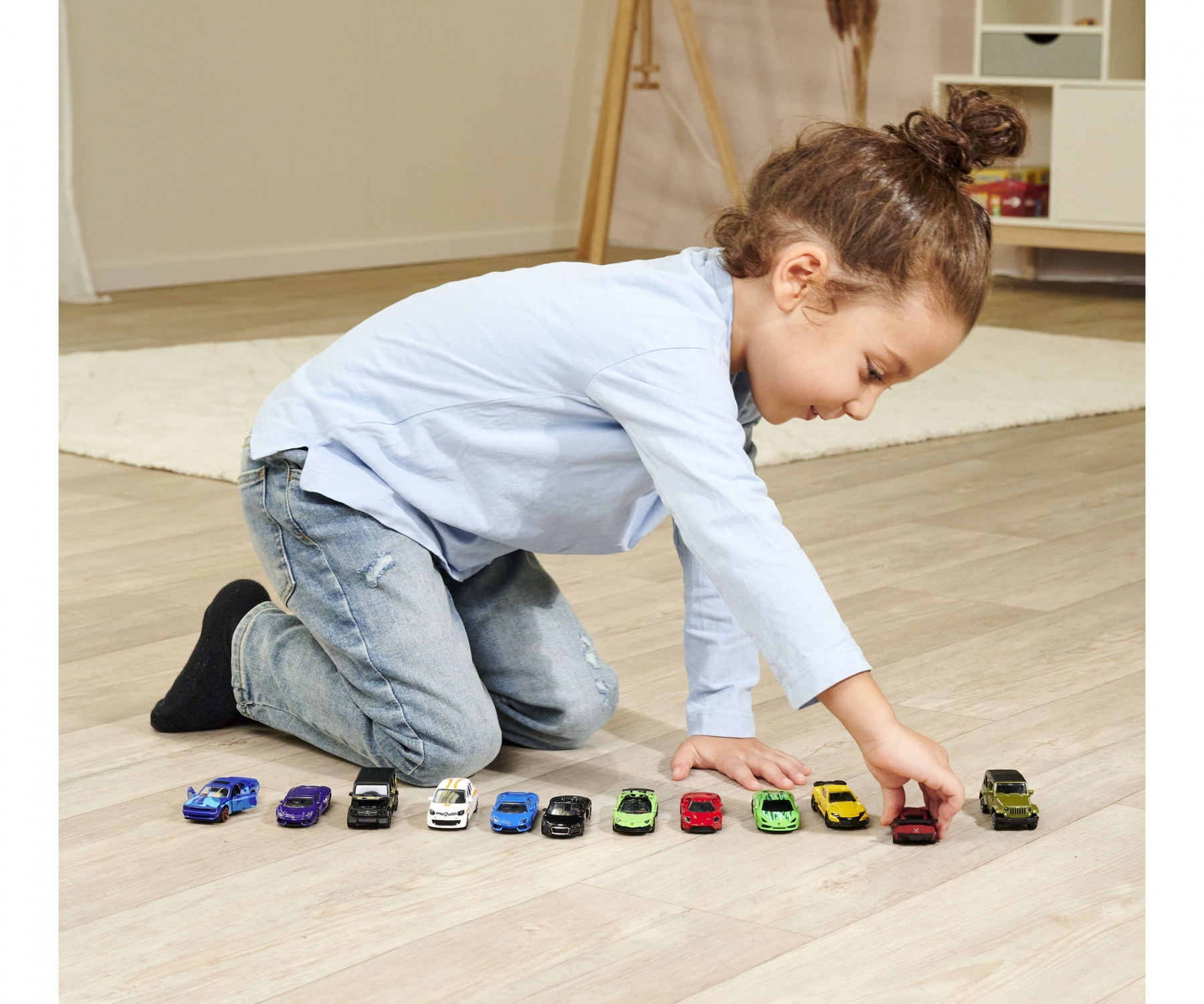 Dziecko klęczy, patrząc na zabawki samochodowe na podłodze. Różne samochody są ułożone.
