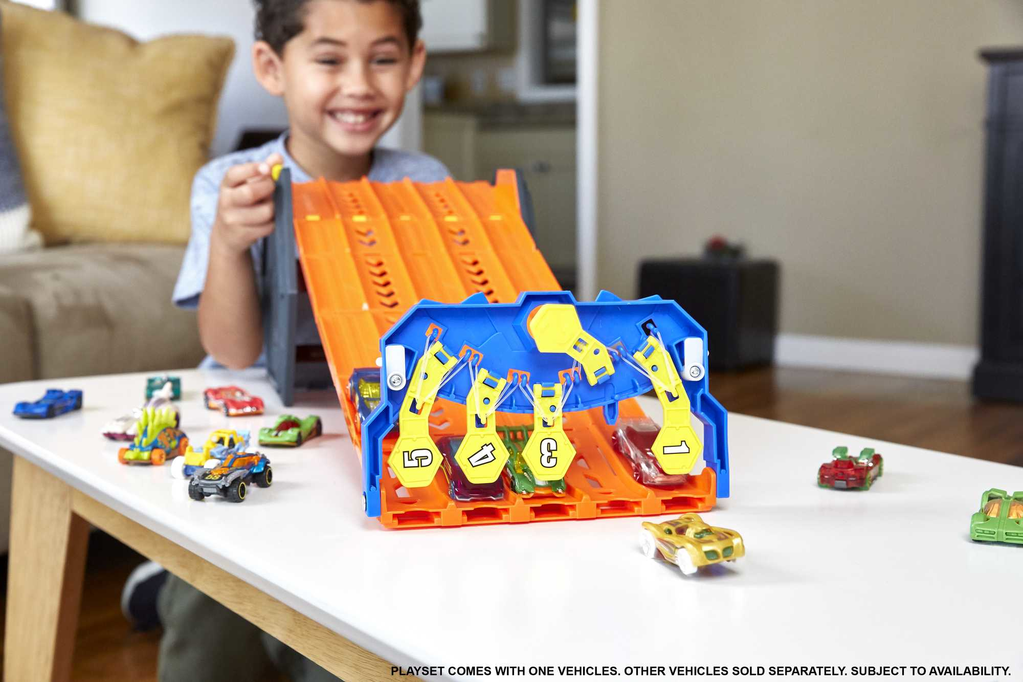 Mały chłopiec uśmiecha się do zestawu torów wyścigowych Hot Wheels z wieloma samochodzikami.