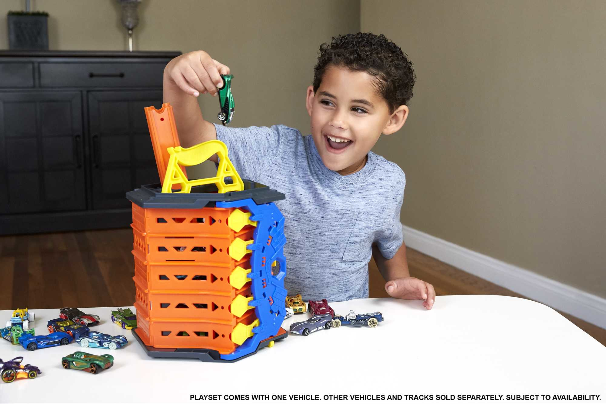 Dziecko bawi się zestawem samochodzików, który zawiera wieżę, rampy i różne zabawki.