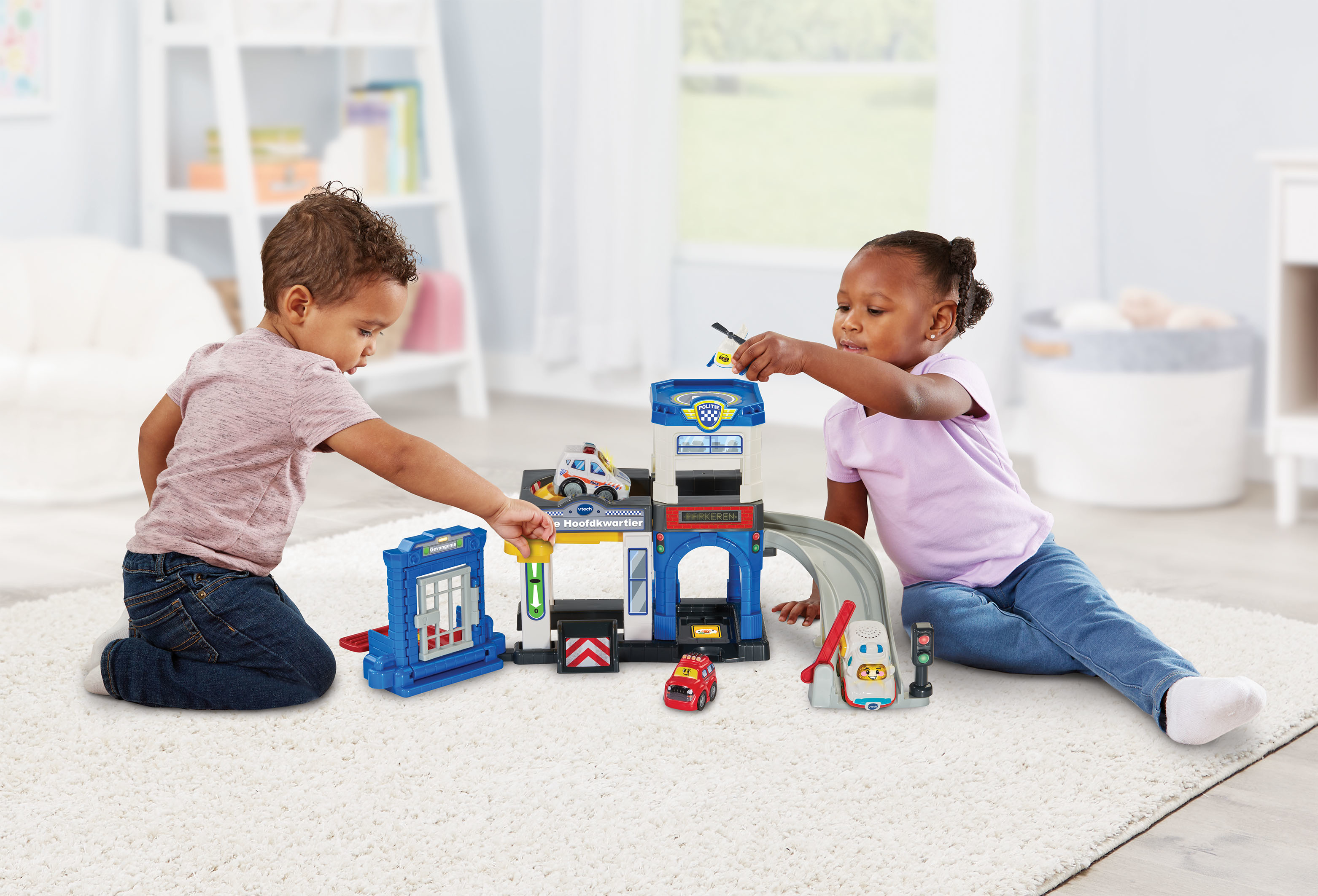 Due bambini che giocano con una stazione di polizia giocattolo. Il set ha garage, rampa ed edifici. Include macchinine e figure.