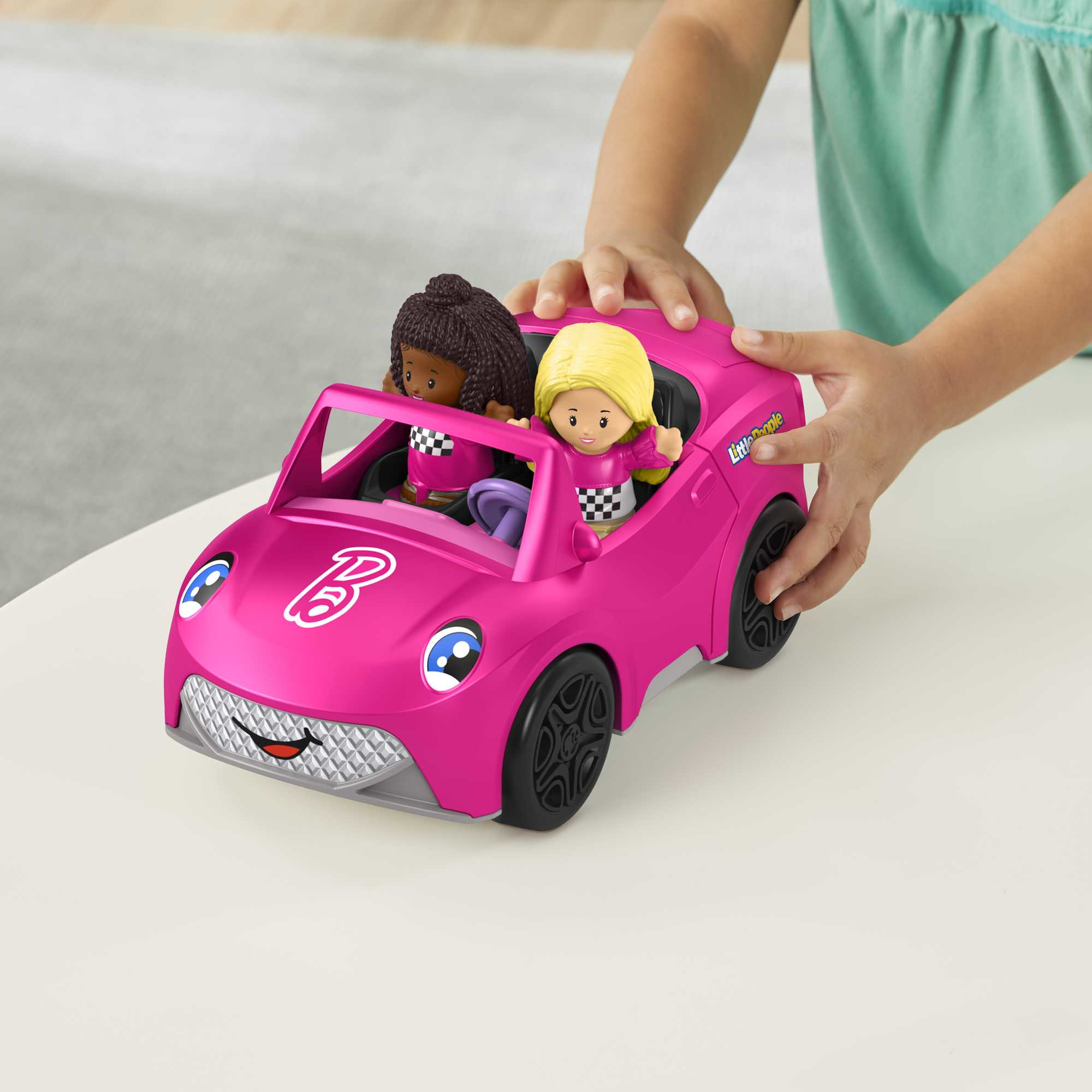 Una niña juega con un coche de juguete rosa con dos muñecas sentadas dentro. El coche está en una mesa.